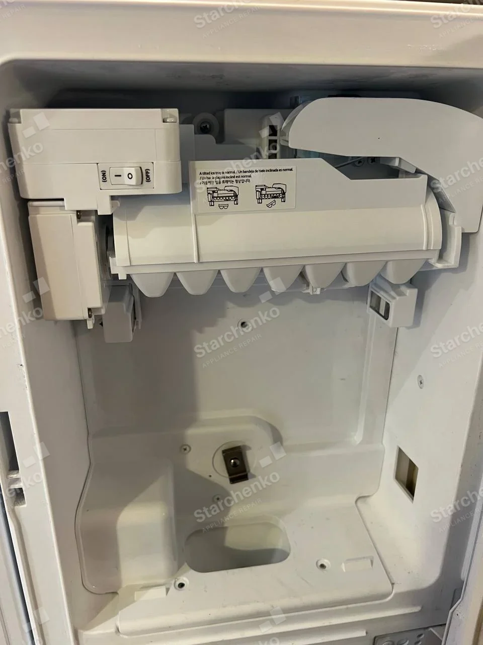 LG repair: Freezer-door ice dispenser recess with installed ice maker assembly and switch visible.