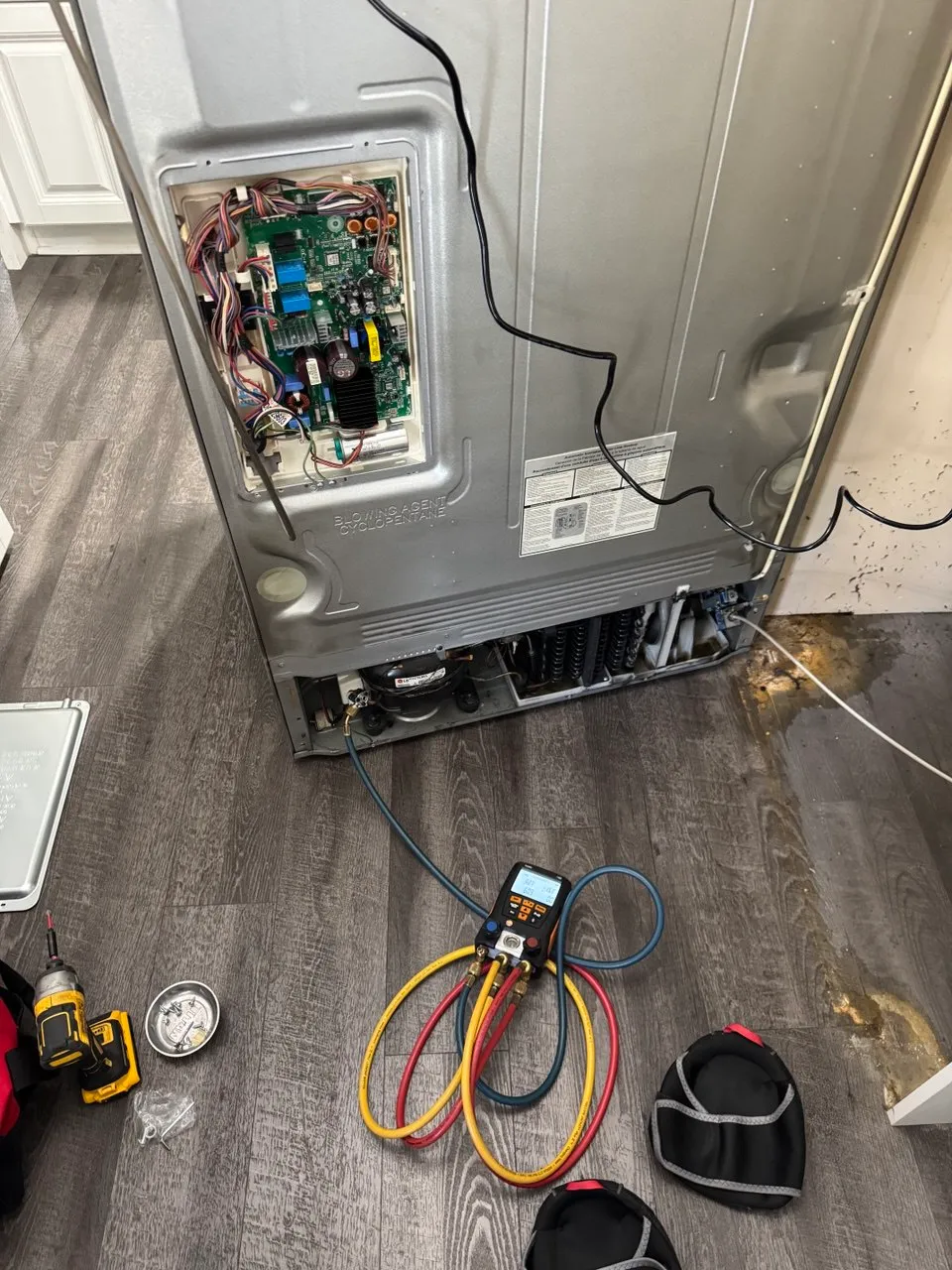 Back of a refrigerator opened for repair with gauges hooked up by the compressor