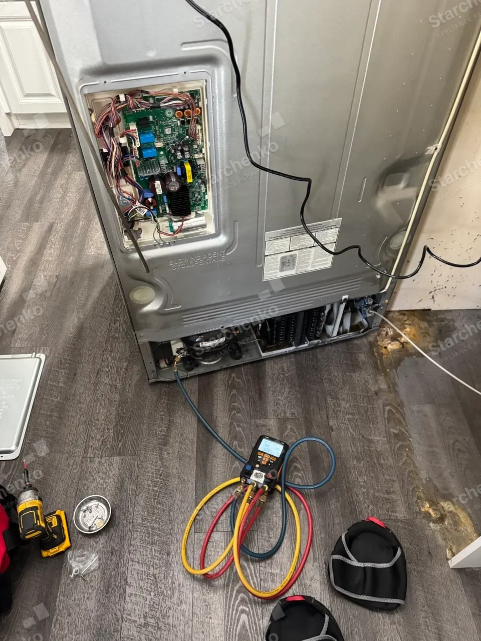 Back of a refrigerator opened for repair with gauges hooked up by the compressor