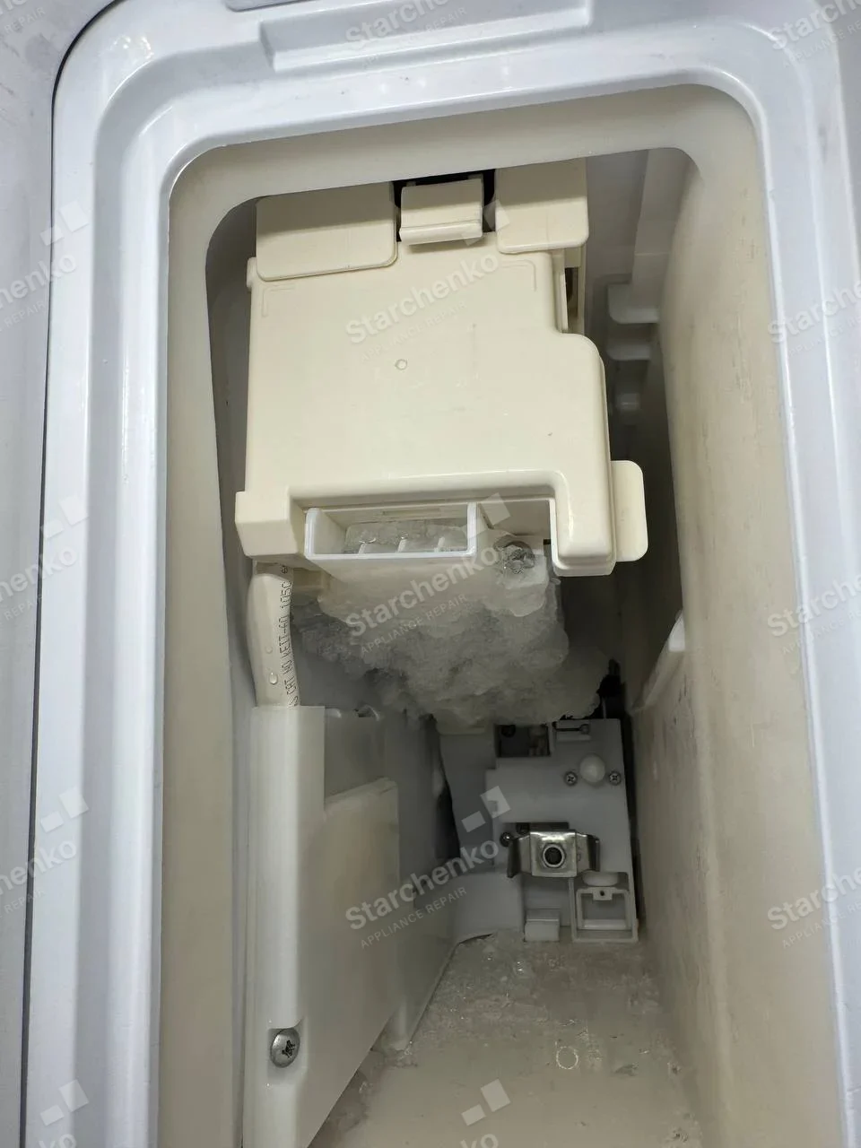 Whirlpool repair: Close-up of frosted ice-making chute and mechanical housing, whole host appliance not shown.