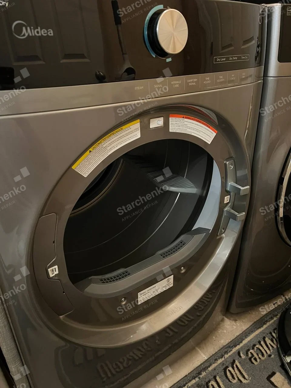 Midea name printed on the dryer's upper-left control panel, front opening exposed with door removed.