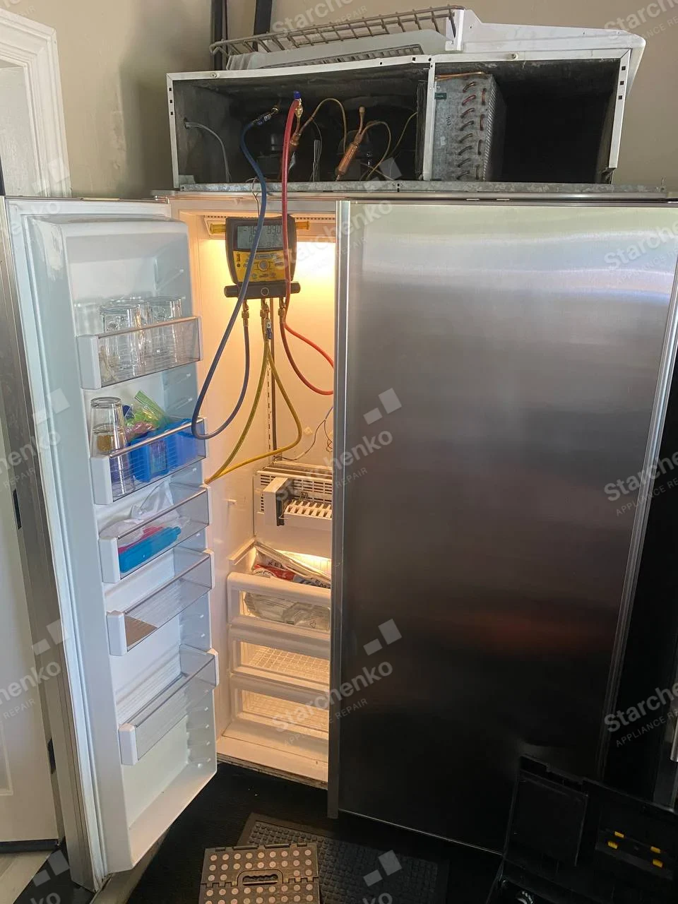 Miele repair: Built-in side-by-side refrigerator with fresh-food door open and top refrigeration service compartment exposed to manifold gauges.