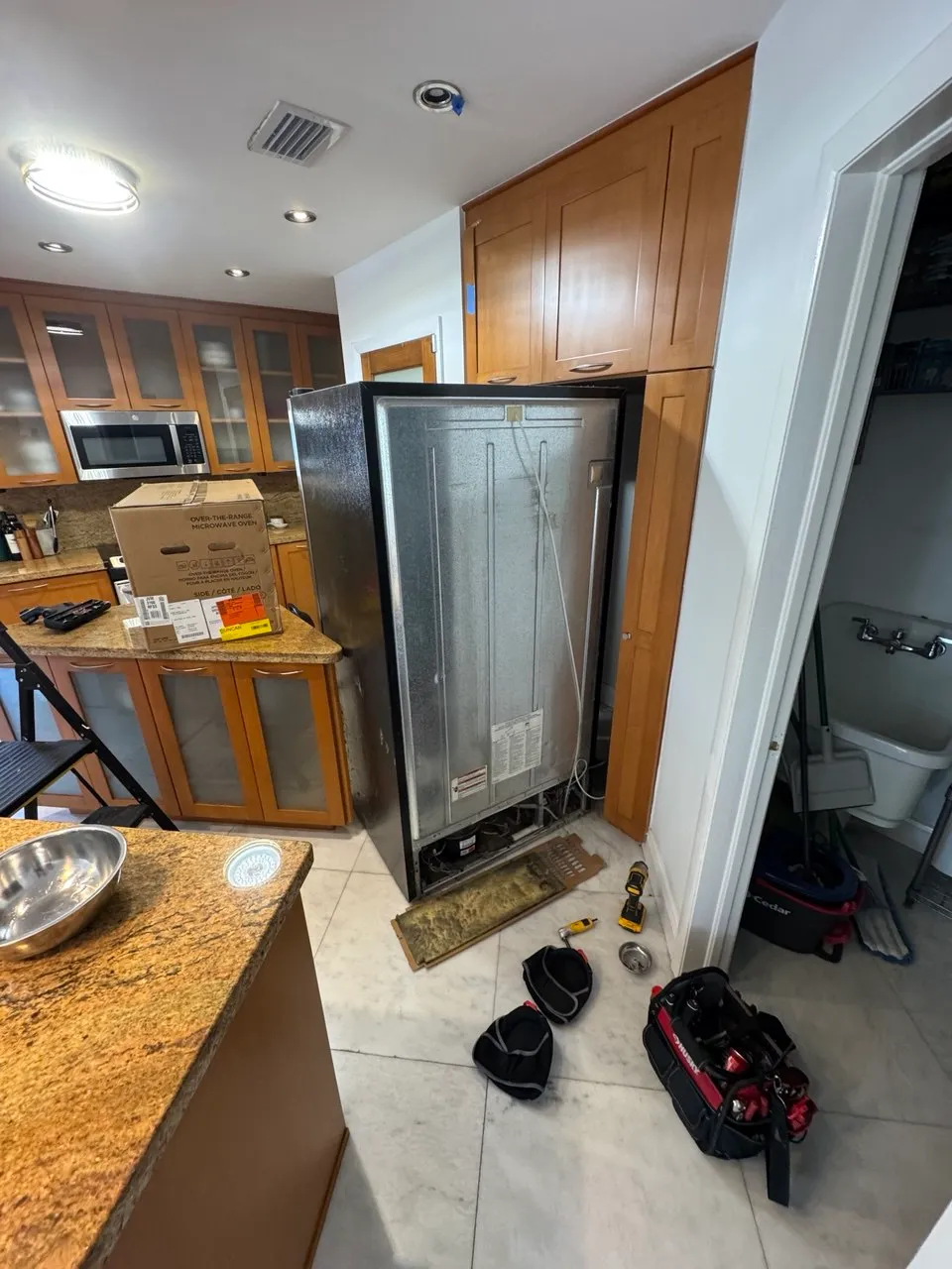 Black refrigerator pulled away from the wall with the rear cover opened