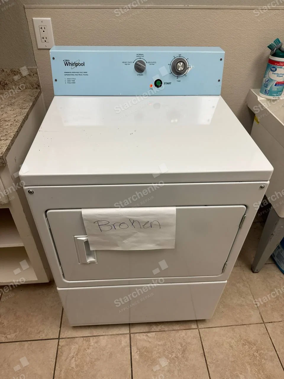 Whirlpool Commercial repair: White front-loading commercial dryer with timing controls and handwritten broken notice taped on door.