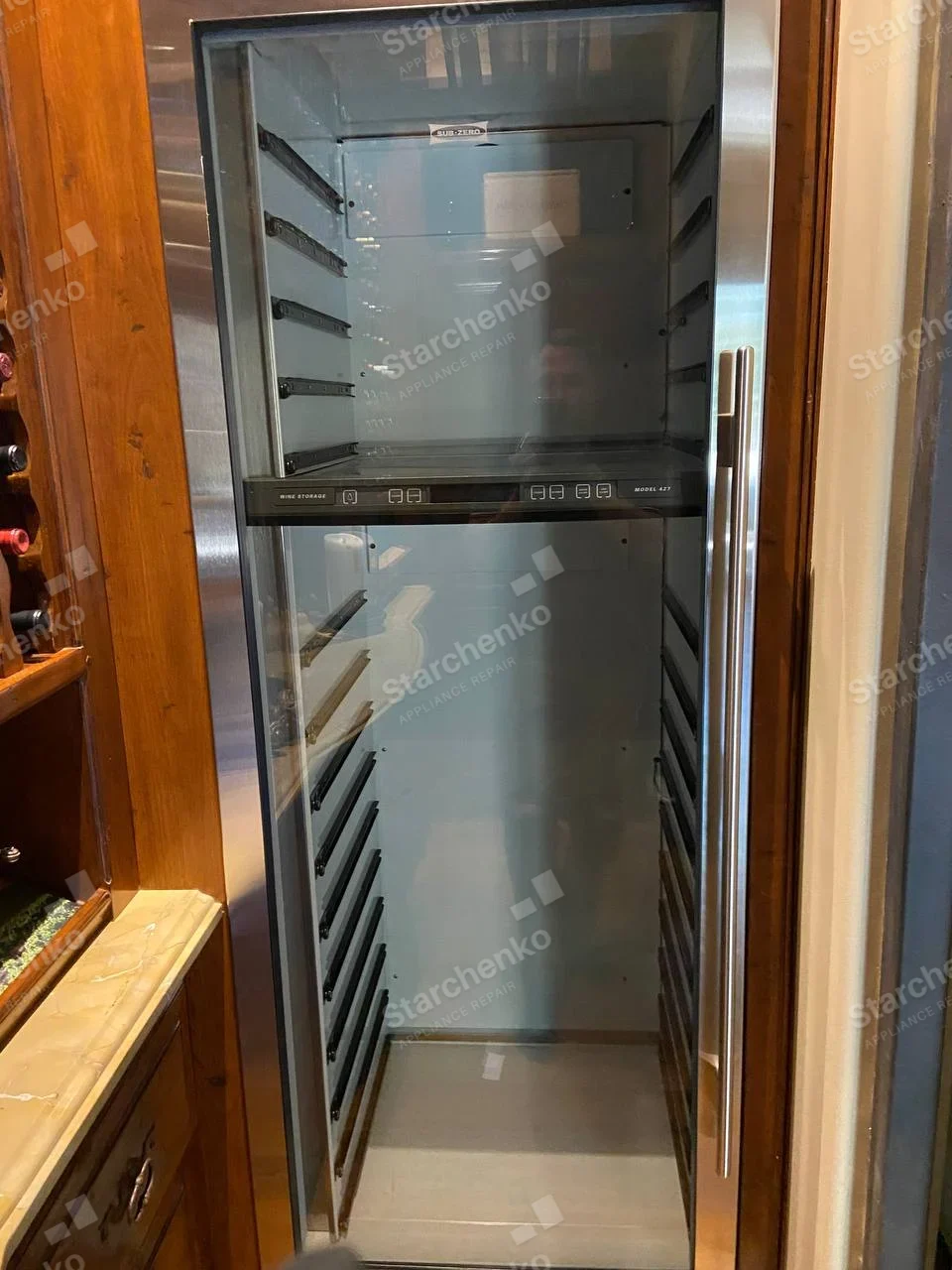 Open Sub-Zero wine storage cabinet with glass door and empty bottle rails.