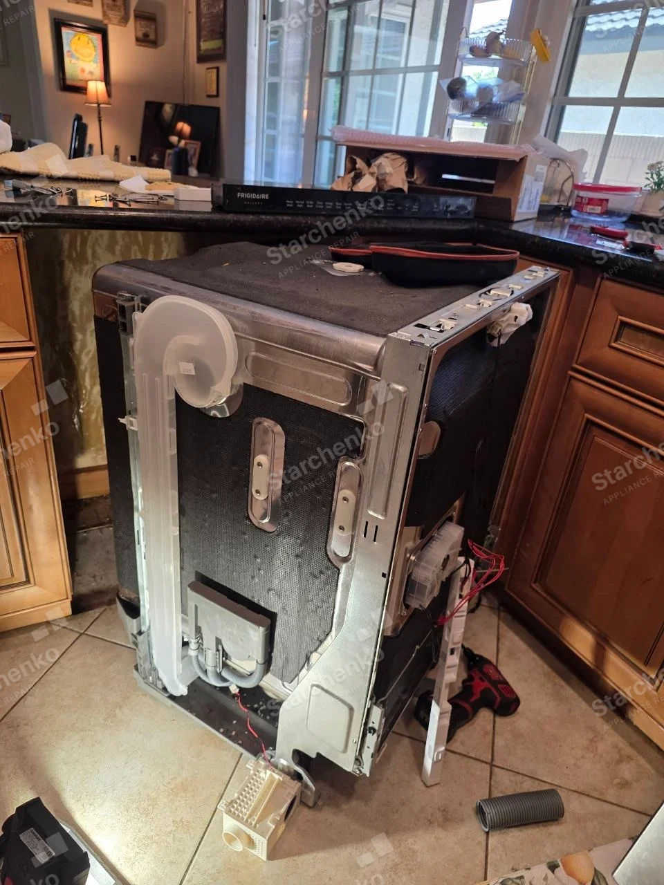 Removed dishwasher has exposed rear/side components, FRIGIDAIRE is printed on its detached top control strip resting on the counter immediately behind the unit.