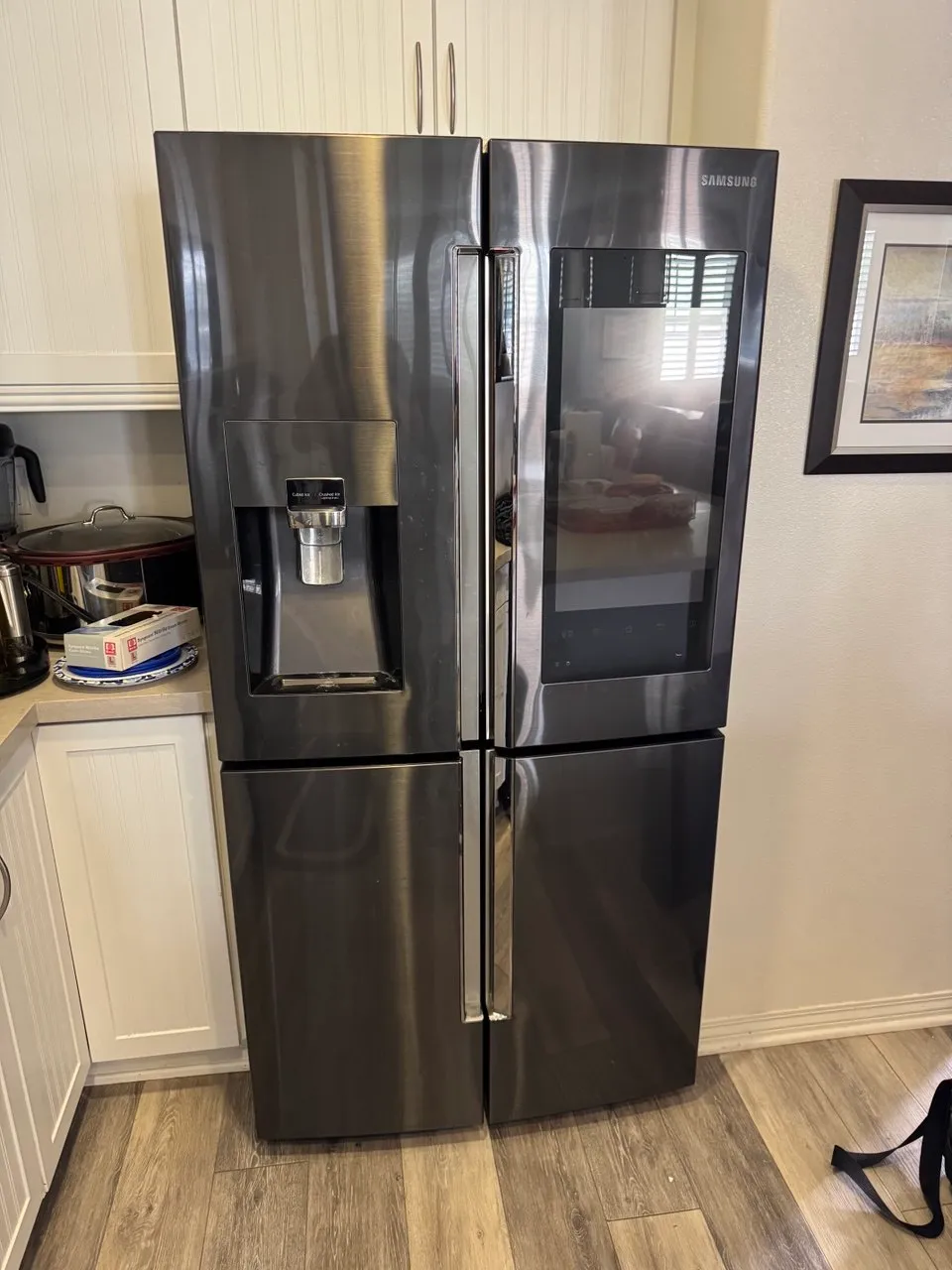 Black stainless Samsung four-door refrigerator in a wood-floor kitchen
