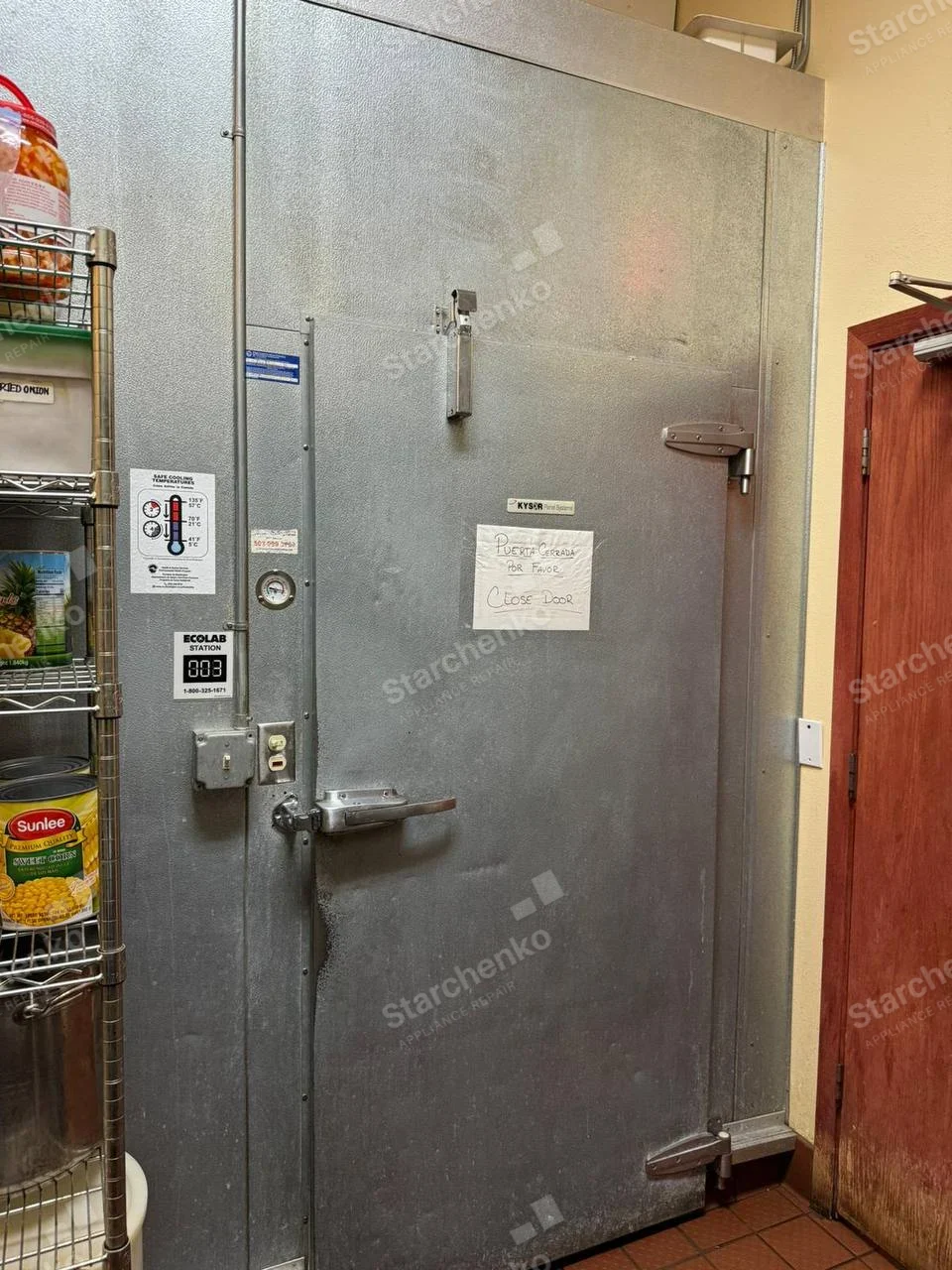 Nor-Lake repair: Large walk-in cooler door with temperature gauge in restaurant storage area, Kysor label appears on door and may identify door maker rather than refrigeration system.