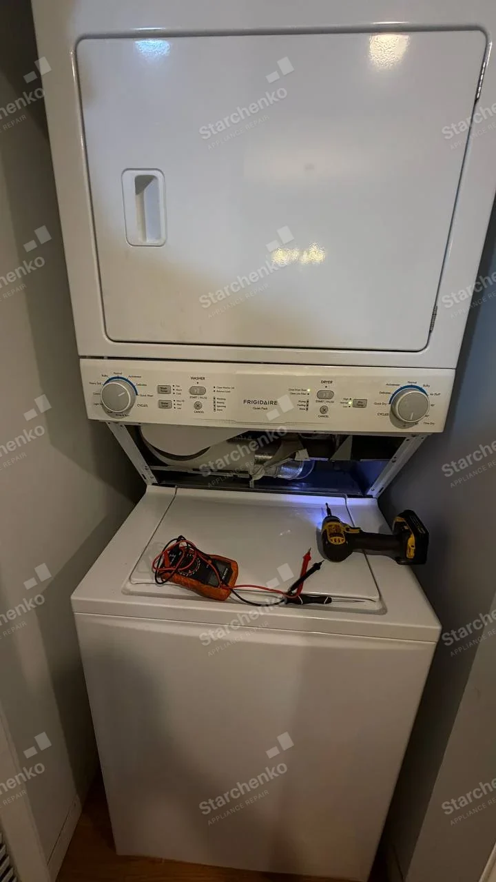 FRIGIDAIRE on shared control fascia, service opening is the lower compartment of the upper dryer, above the washer top, with dryer drum/drive visible.