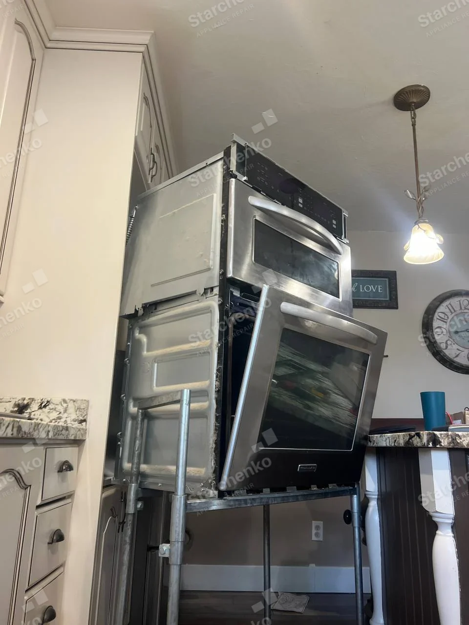 Whirlpool repair: Built-in combination with upper microwave and lower oven, pulled out on wheeled stand with lower oven door ajar, badge too small to read.