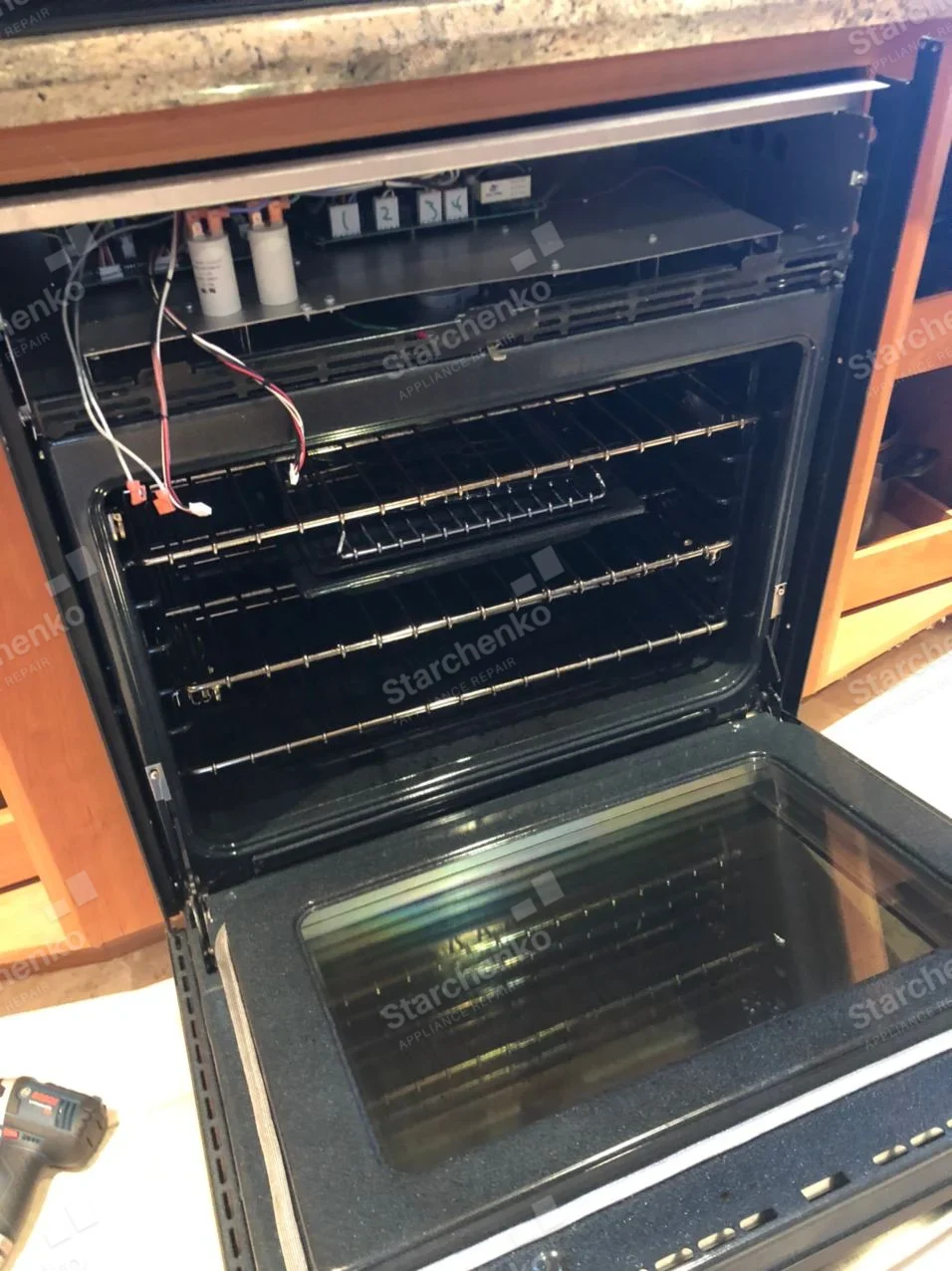 Whirlpool repair: Open built-in wall oven with upper control panel removed and connectors hanging above cavity.