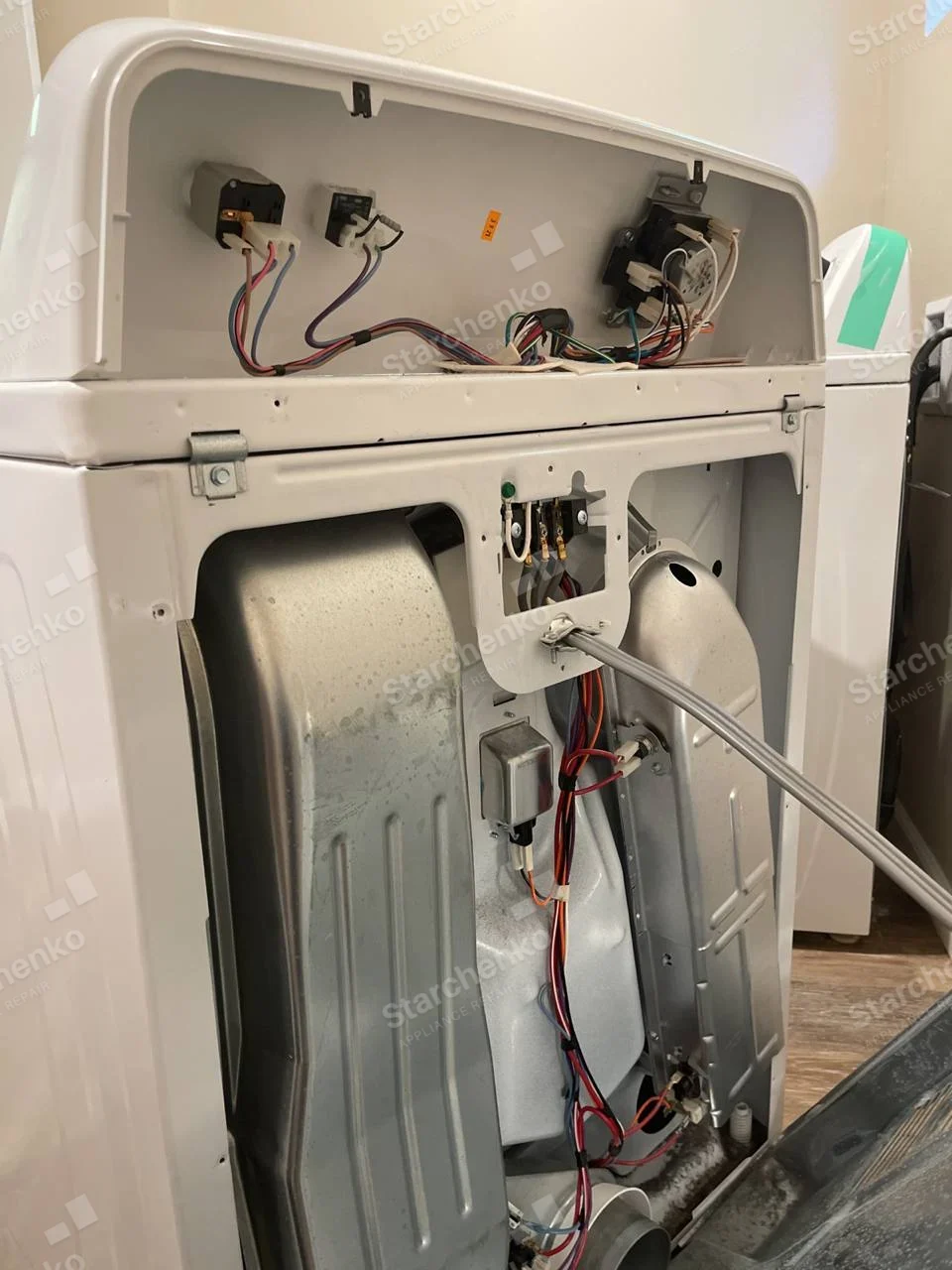 Whirlpool repair: Rear of clothes dryer with back panel removed, exposing drum housing and wiring.