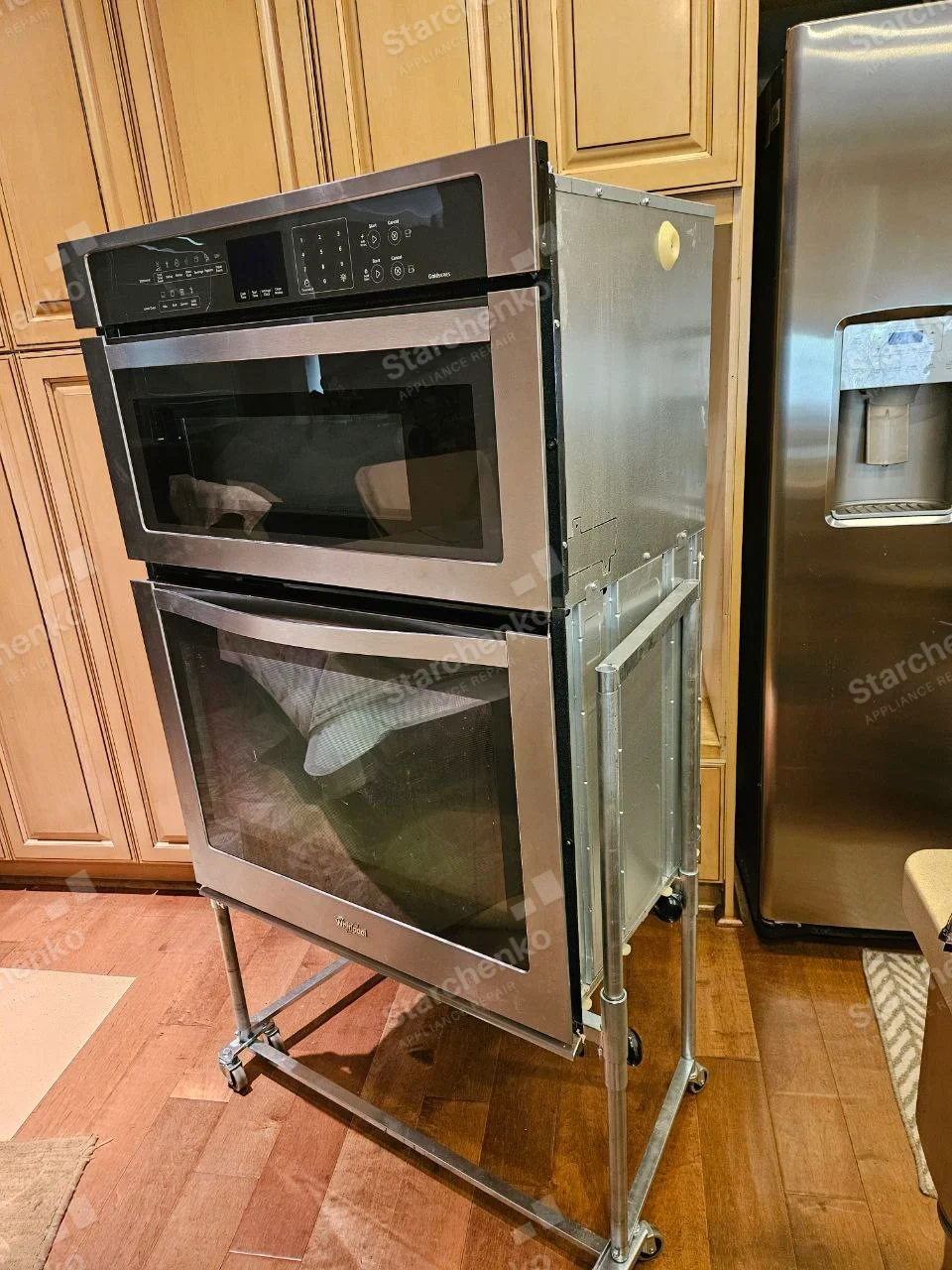 Whirlpool name on lower built-in oven door, combined microwave above on service stand, separate refrigerator adjacent.