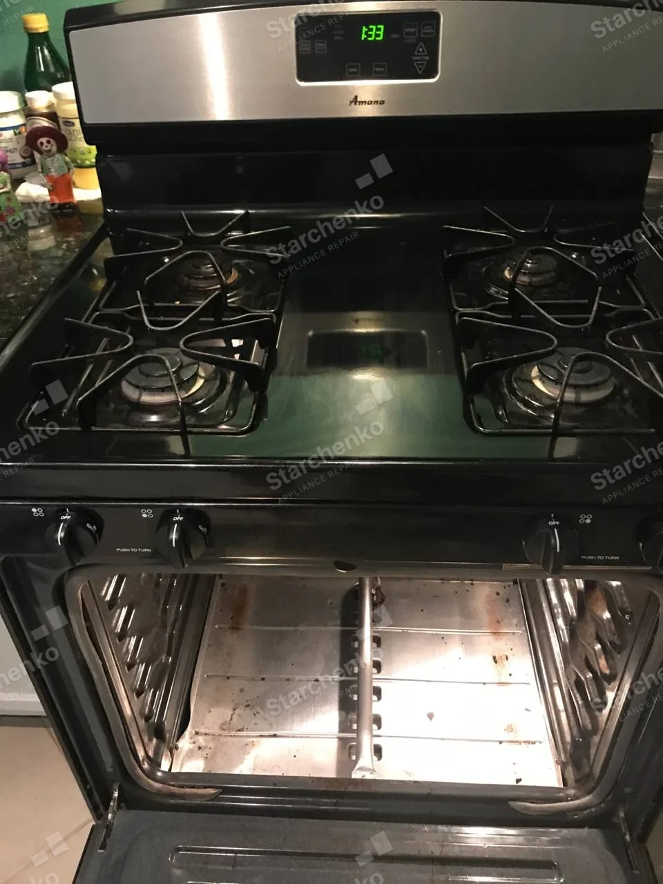 Amana four-burner gas range with oven door open and bottom oven panel removed.