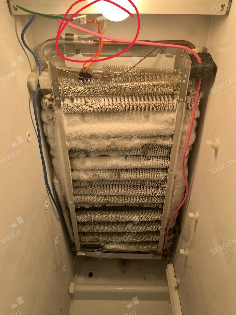 Frigidaire repair: Exposed refrigerator evaporator coil coated in frost with defrost wiring and red annotation.