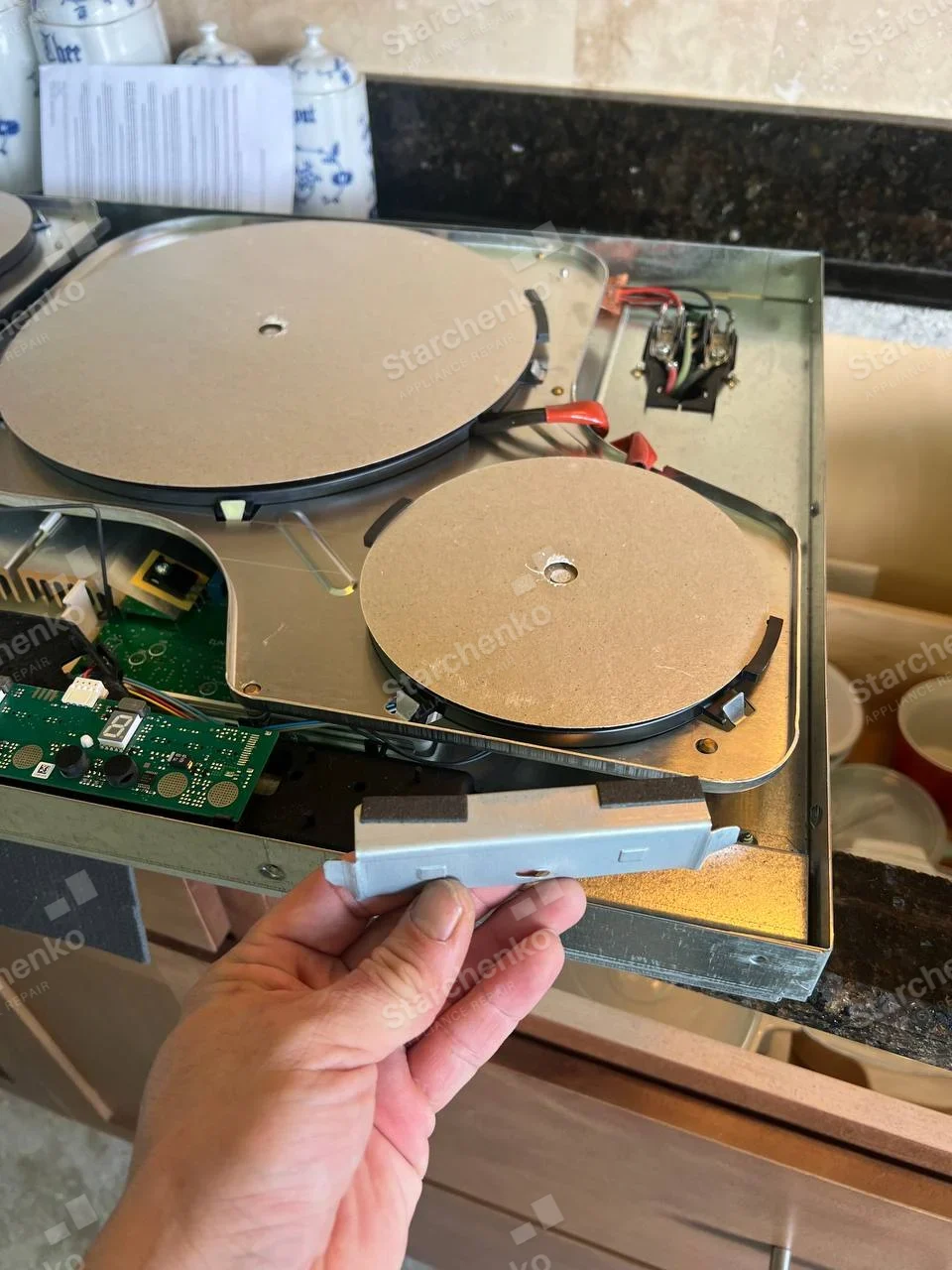 Removed Whirlpool electric two-element cooktop with hot plates and circuit board exposed, technician holds detached component.