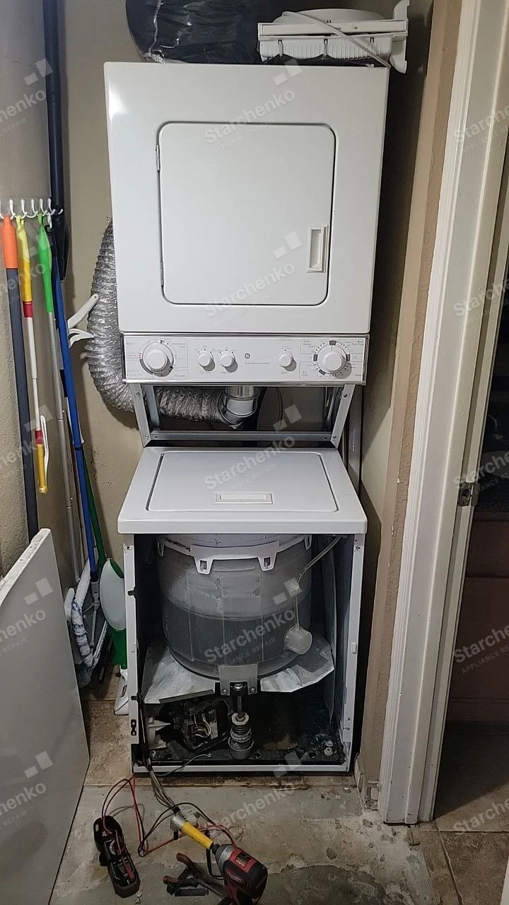 Amana repair: Stacked laundry center with lower washer cabinet removed, exposing tub and suspension below dryer.