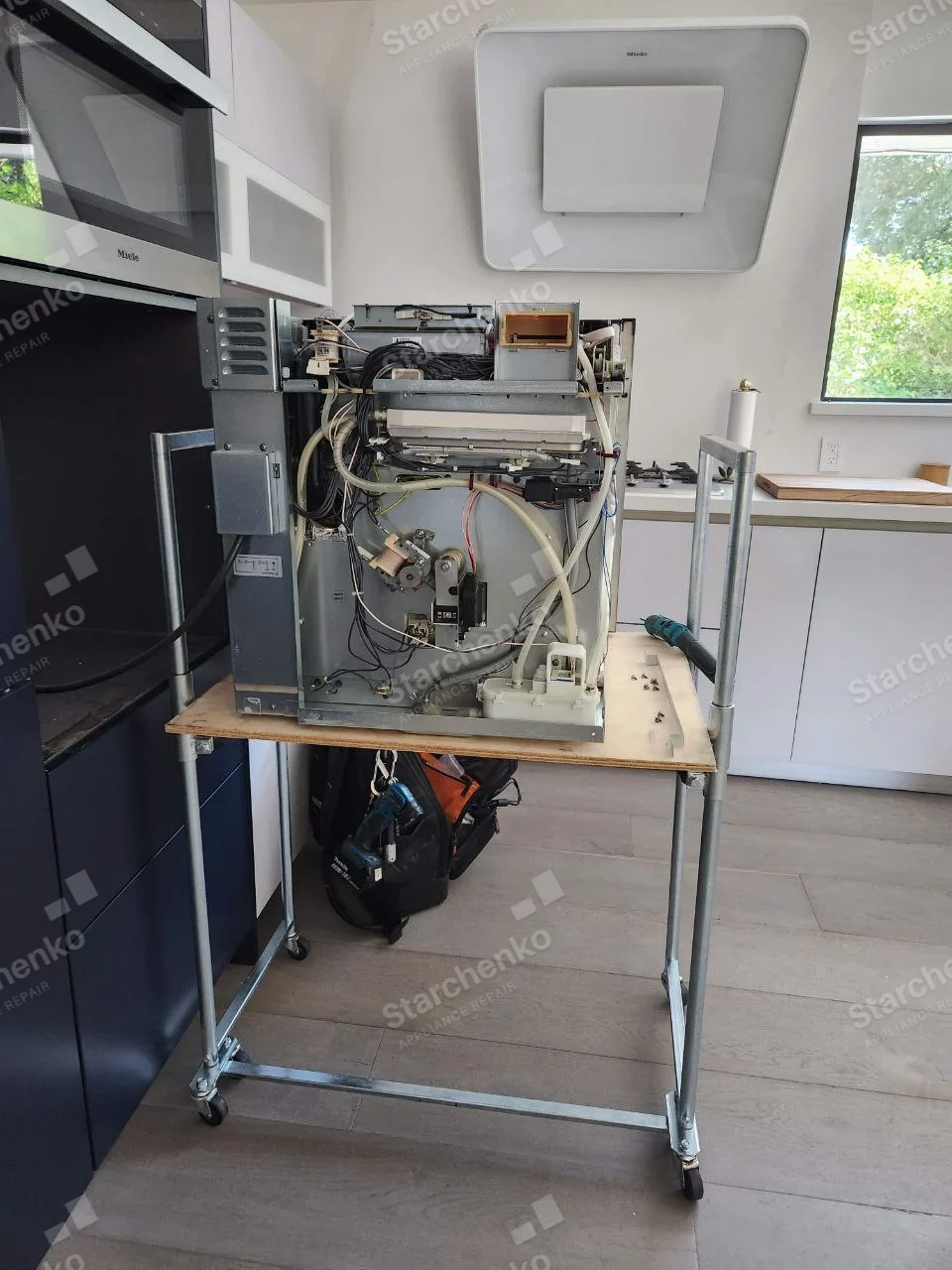 Samsung repair: Dishwasher on service stand with cover removed, exposing pump, hoses and wiring.