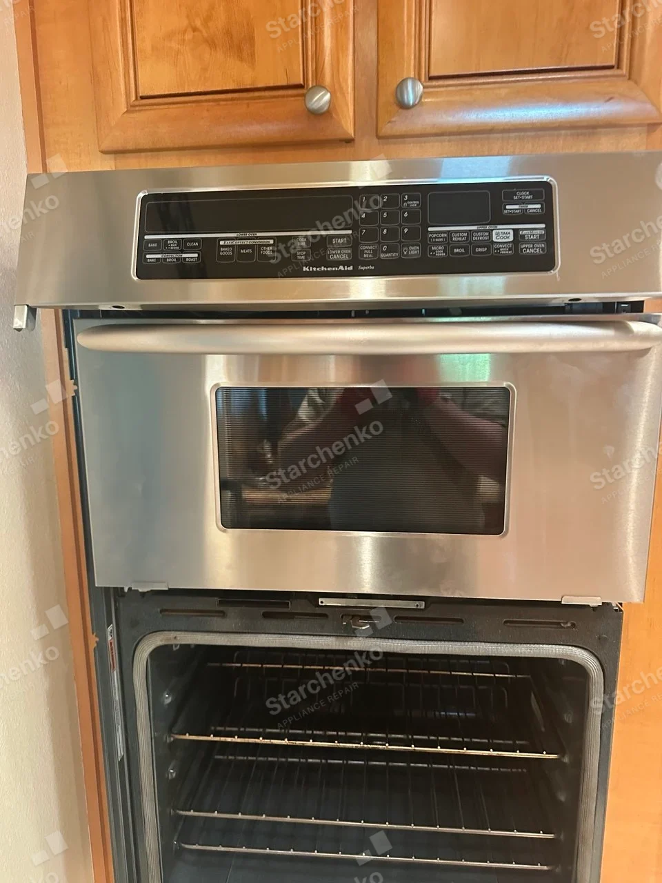 KitchenAid text on central control fascia of built-in upper microwave/lower oven combination, lower oven door open.