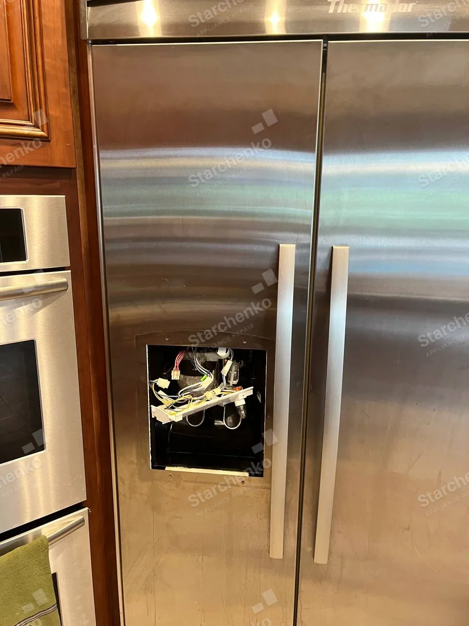 Thermador built-in side-by-side refrigerator with left-door dispenser panel removed, wiring exposed.