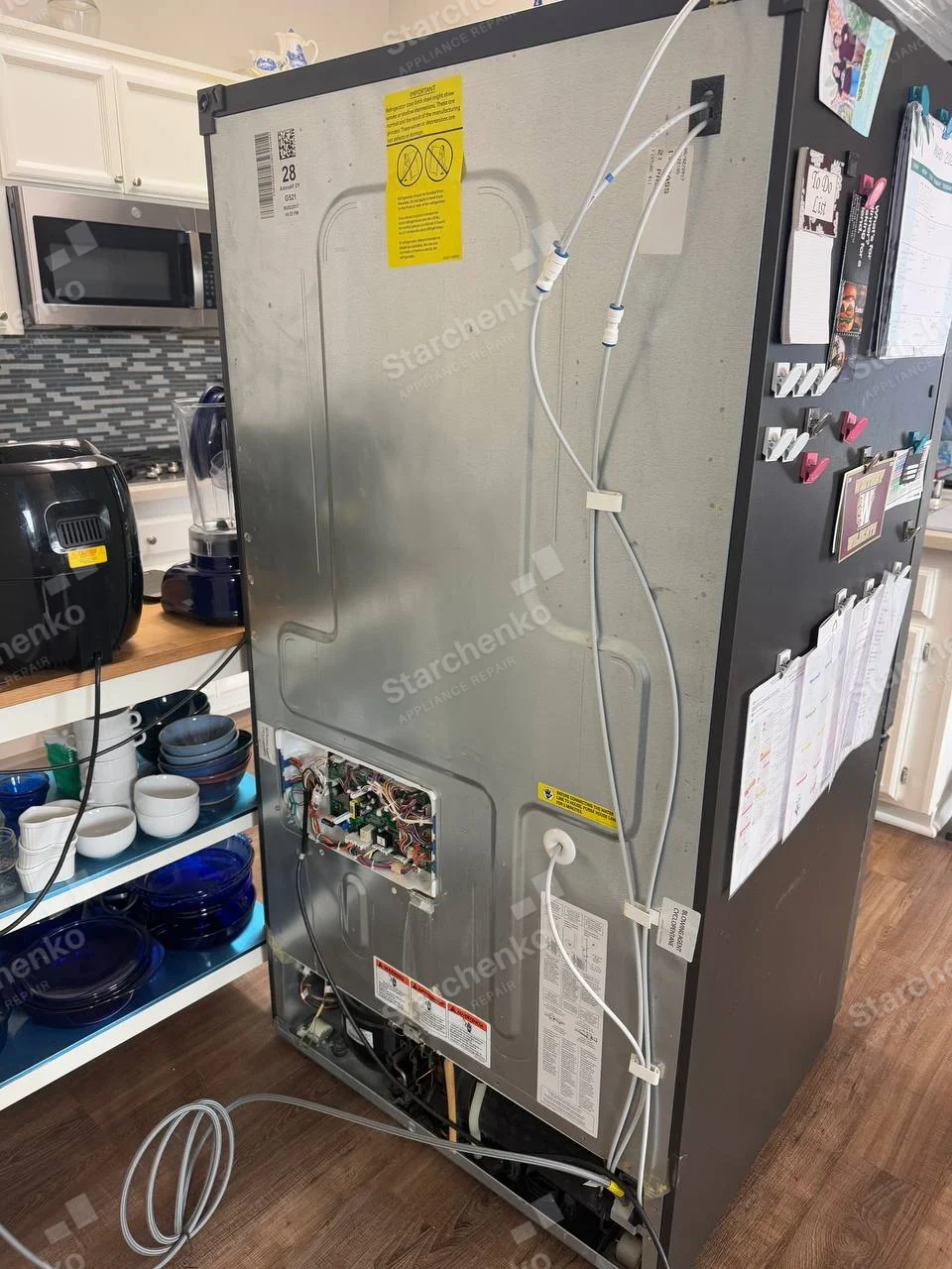 Frigidaire repair: Rear of refrigerator pulled out with lower electronics and water lines exposed.