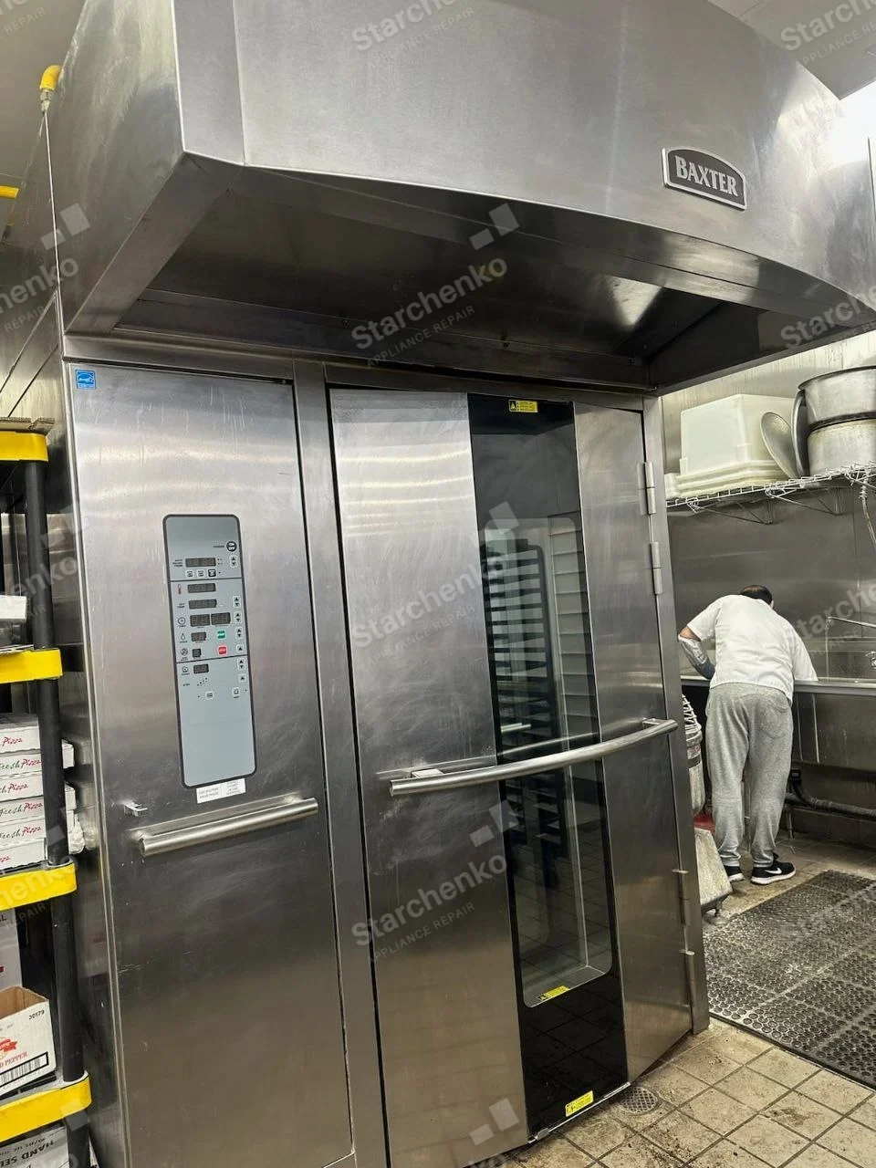 Baxter repair: Large stainless rack oven with glass door and overhead exhaust hood in a commercial kitchen.