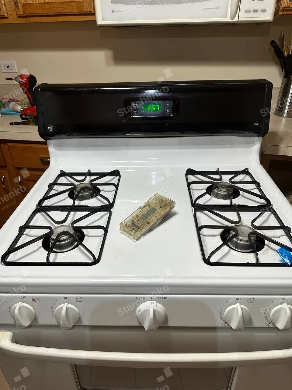 GE round logo on upper-left control fascia of four-burner gas range, loose electronic module on cooktop.