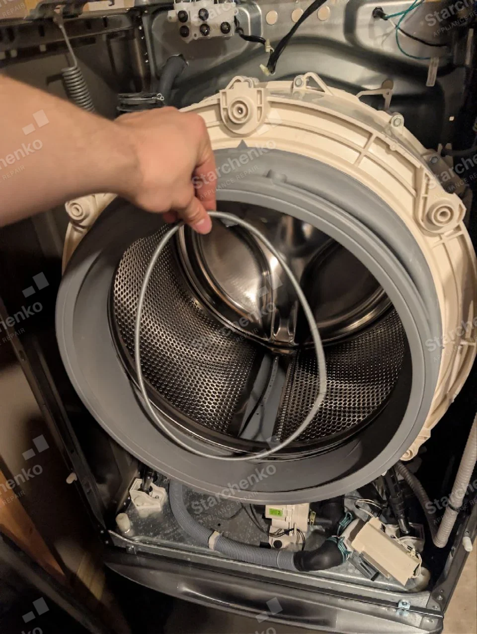 Kenmore repair: Front-load washer front cabinet removed and drum exposed, technician holds retaining wire for door boot.