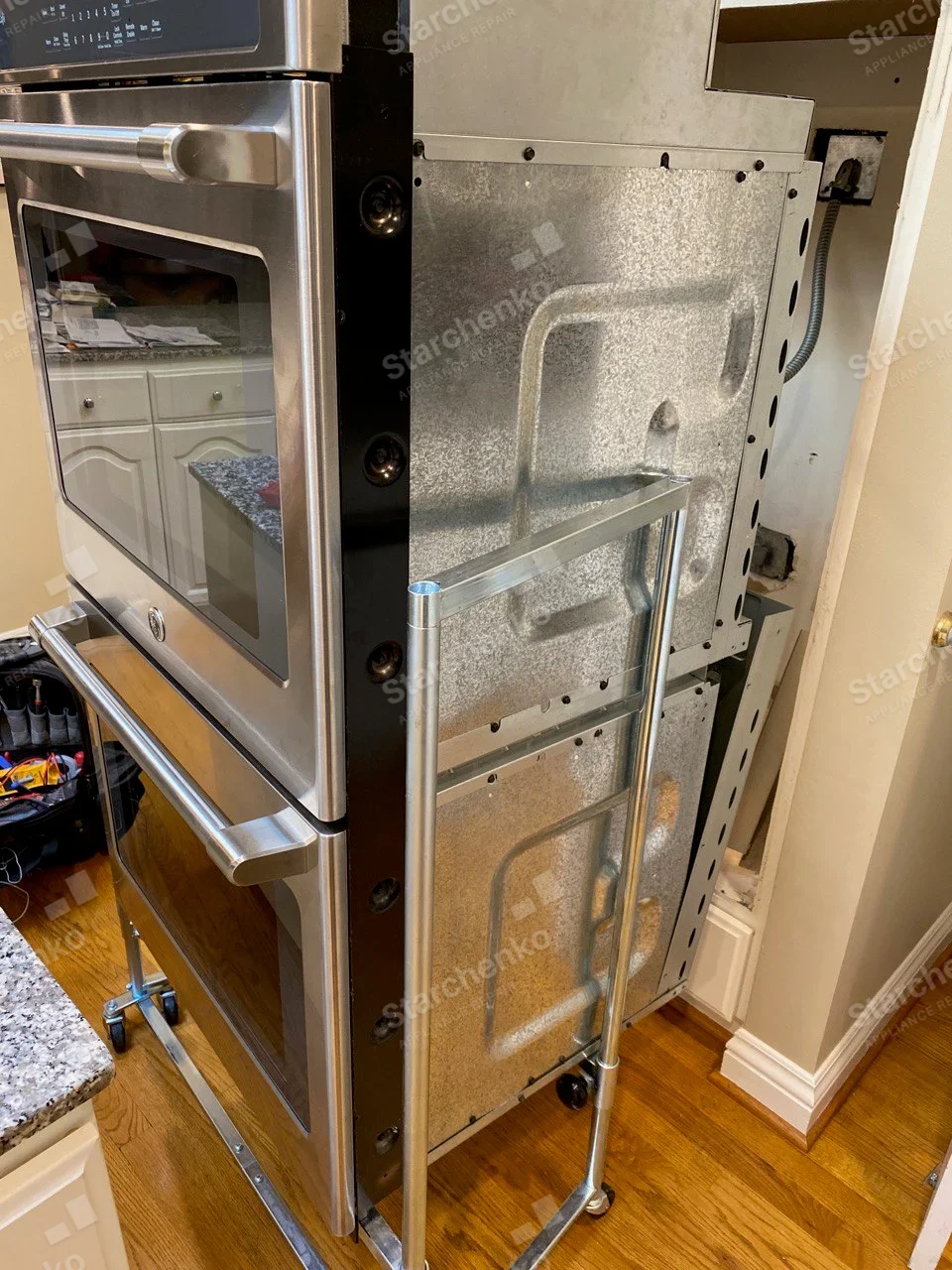 GE stainless double wall oven pulled from cabinet on dolly with side metal enclosure exposed.