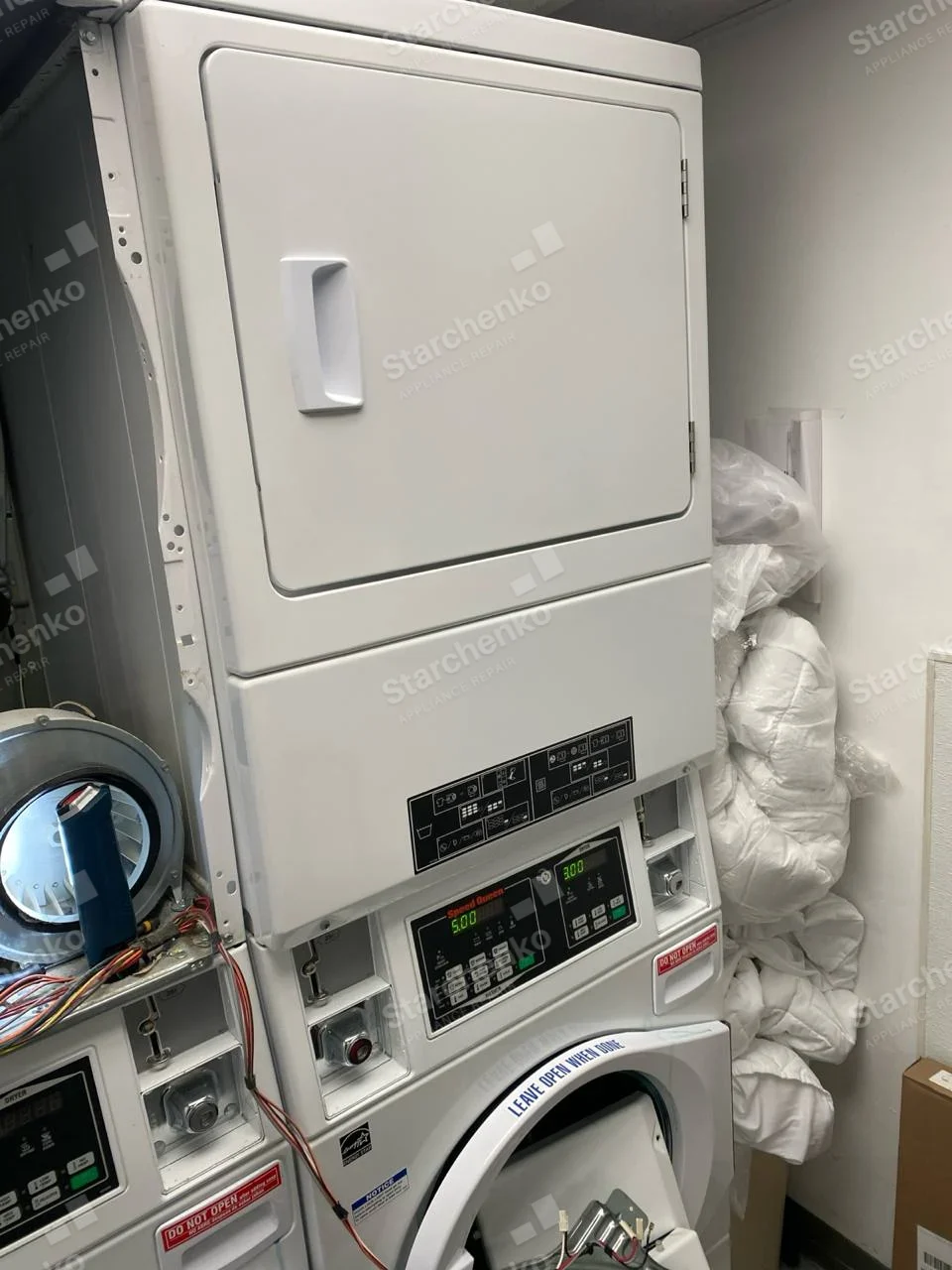 Speed Queen repair: Coin-operated laundry stack, lower front-load washer control panel lit and lower door/service area open, upper dryer closed.