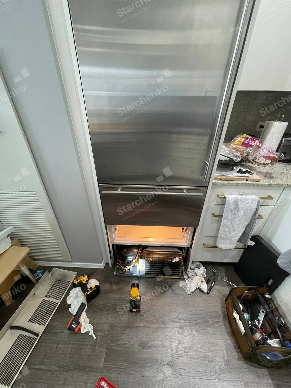 GE Monogram repair: Tall stainless refrigerator with lower grille removed, exposing compressor and condenser coil.