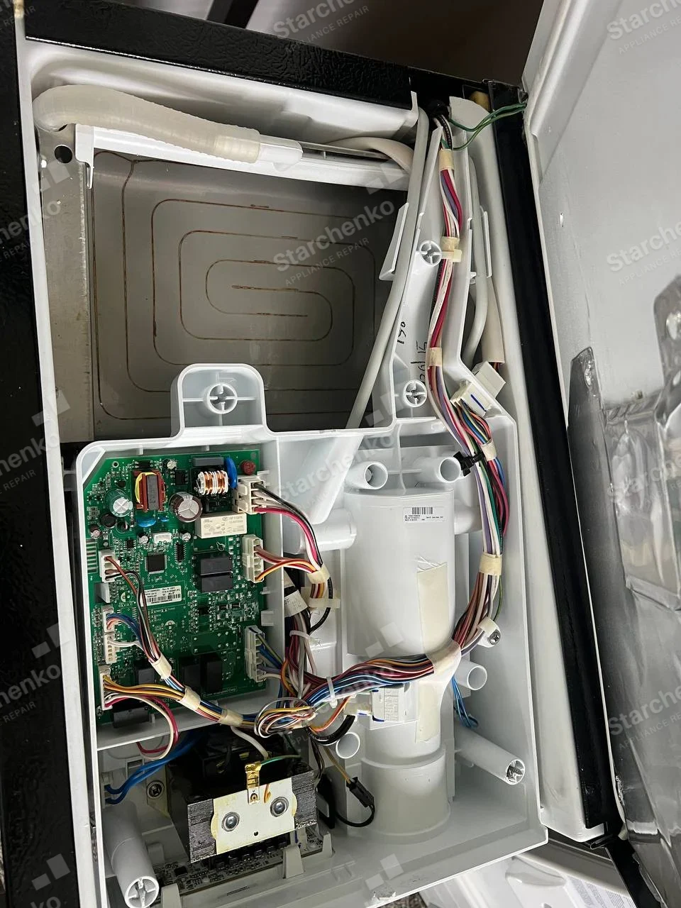 GE repair: Dryer cabinet opened around circuit board and wiring with drum housing and insulated metal panel visible.