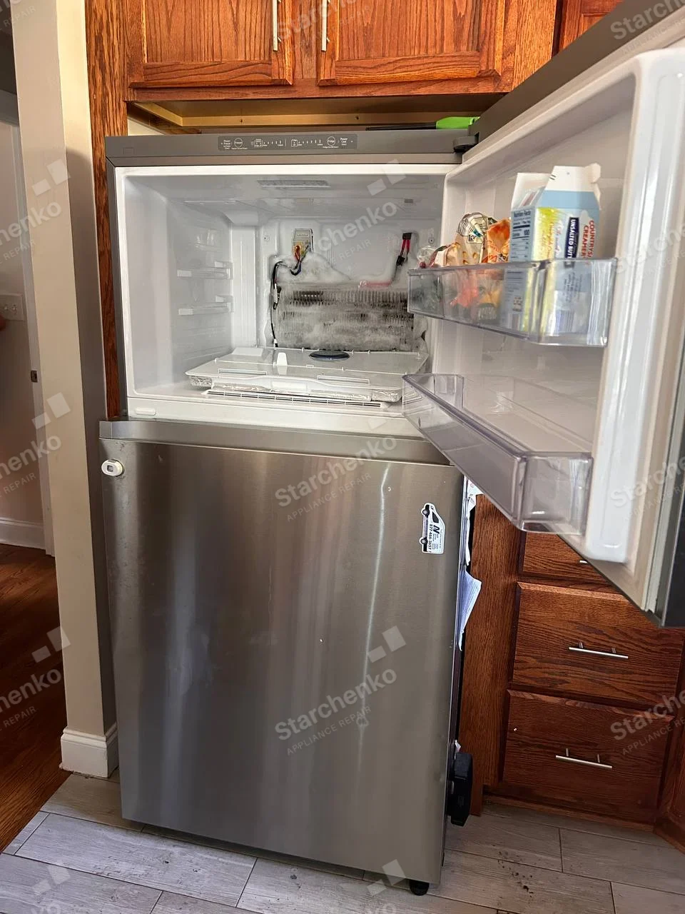 Frigidaire repair: Top-freezer refrigerator with freezer rear liner removed, heavily frosted evaporator and wiring exposed.