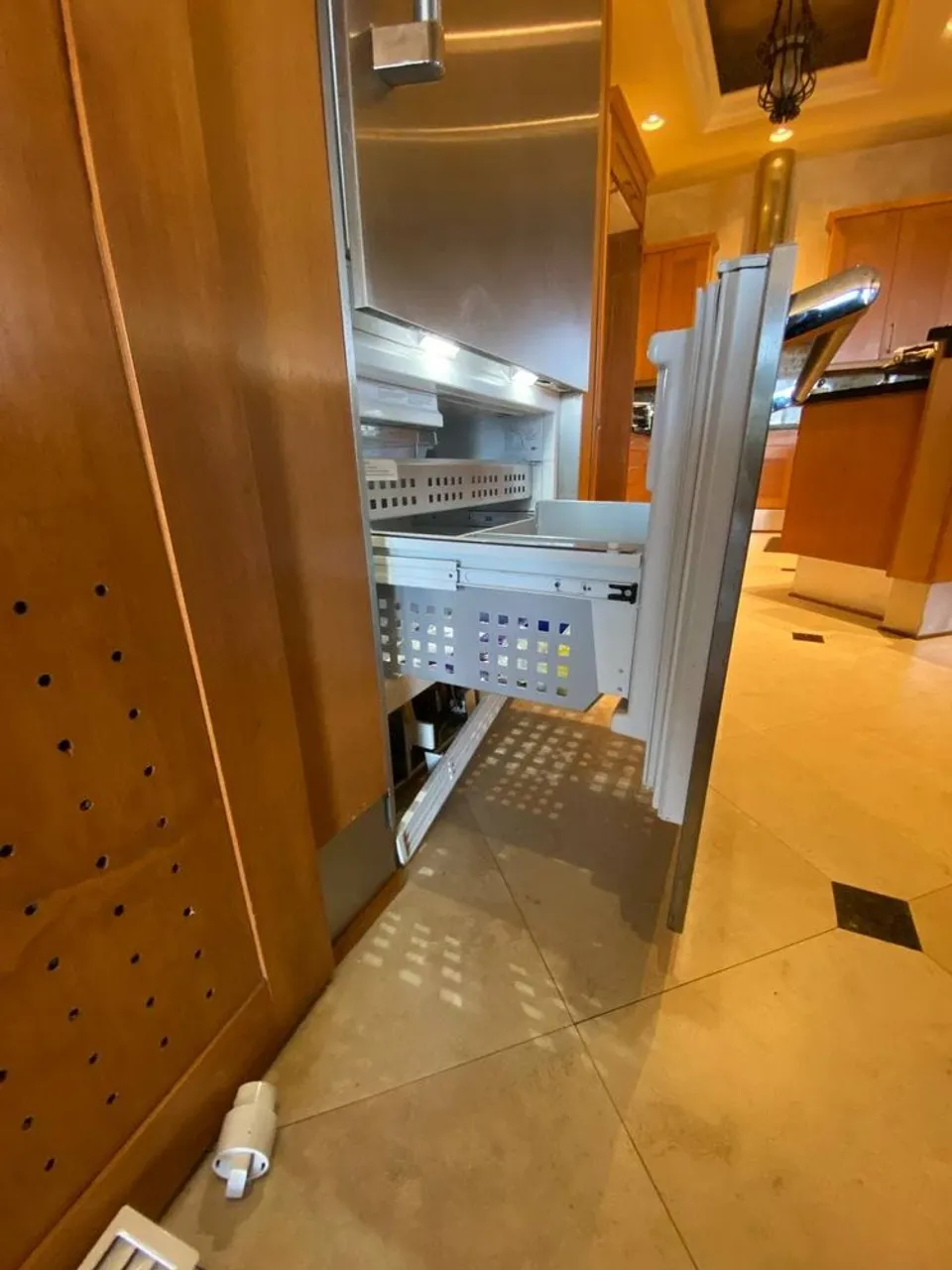 Built-in refrigerator with its door removed during a repair in a wood-paneled kitchen