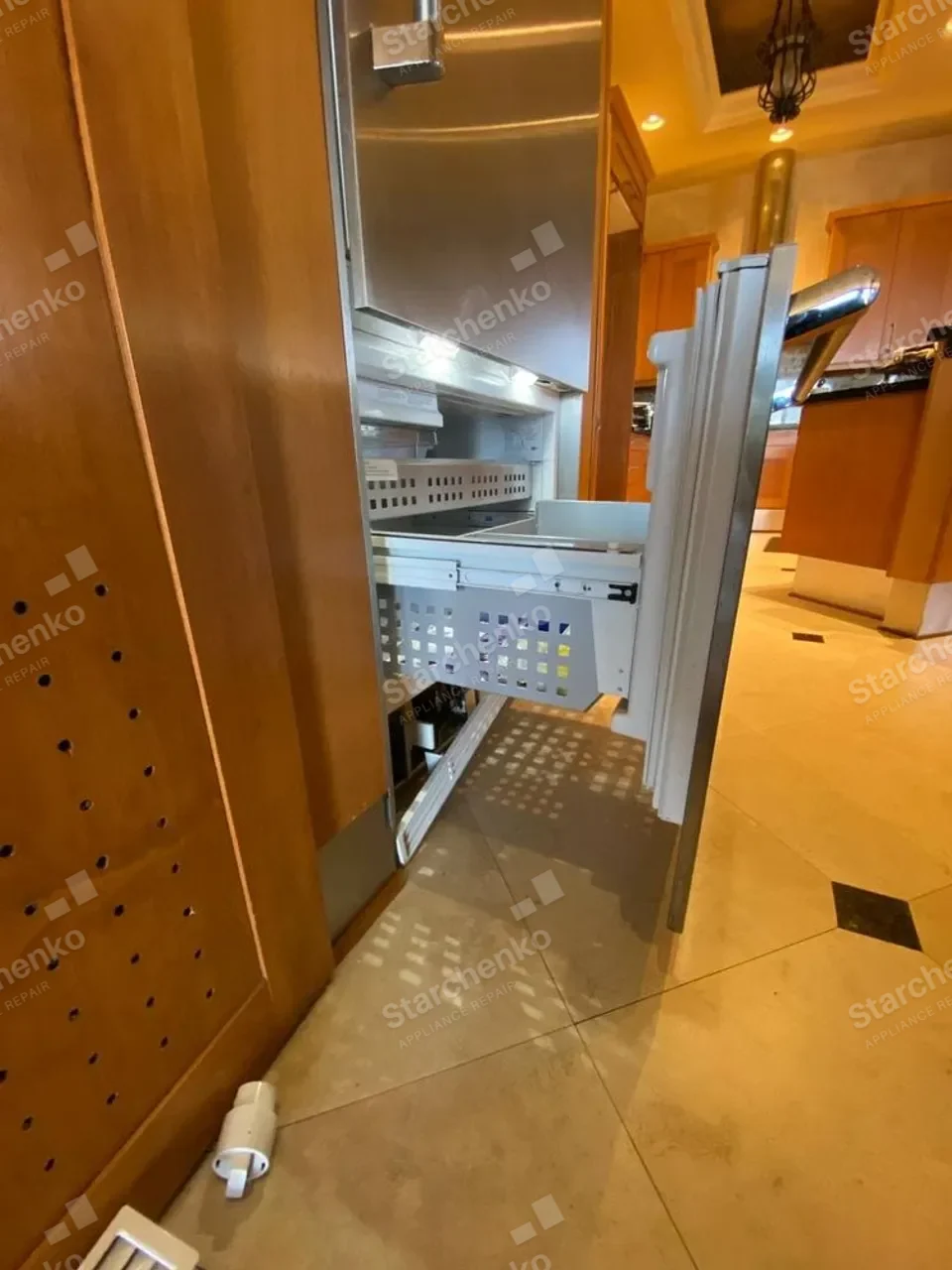 Viking built-in refrigerator with its door removed during a repair in a wood-paneled kitchen