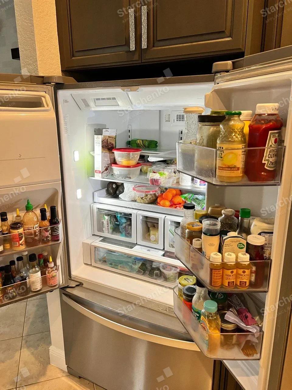 French-door KitchenAid refrigerator open with the shelves and door bins full