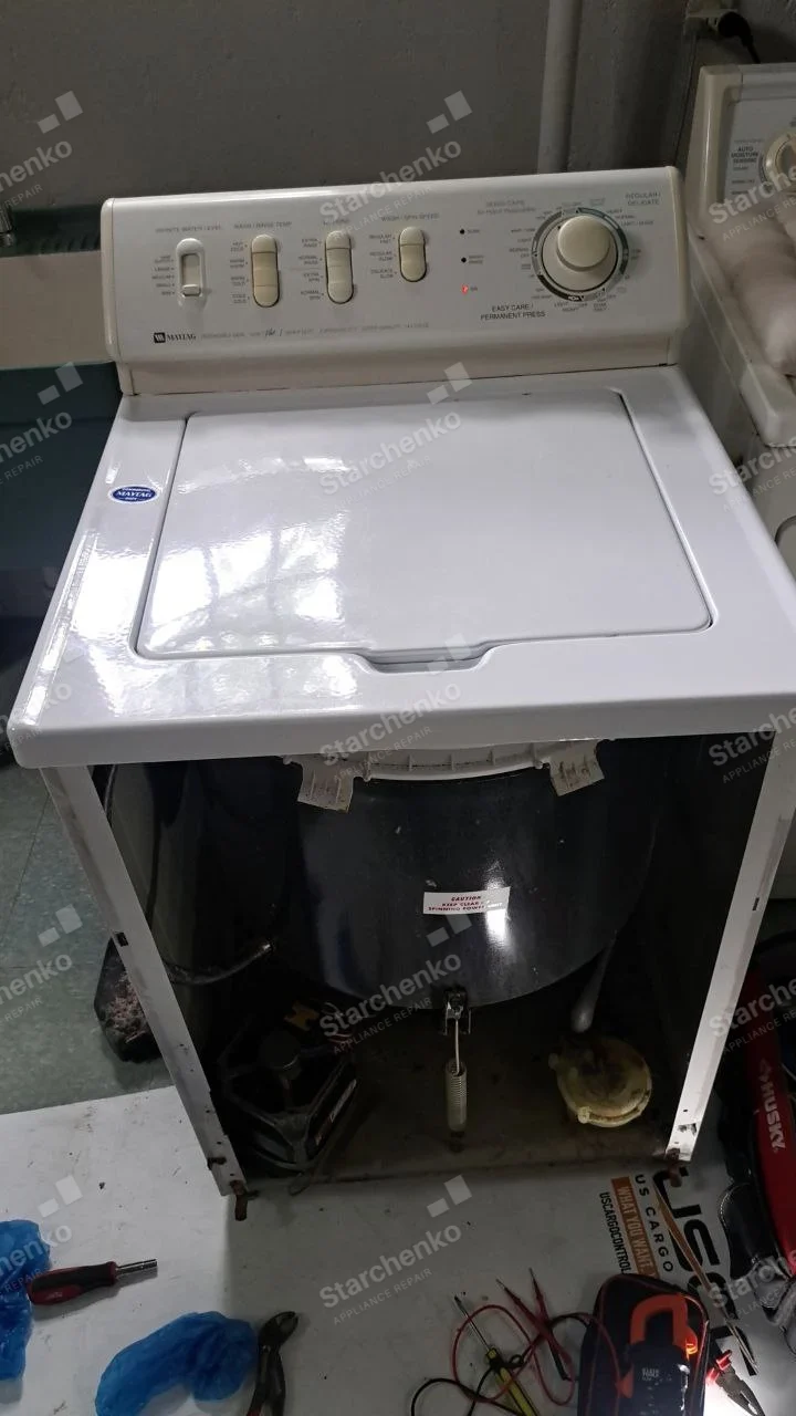 Maytag repair: Top-load washer with front cabinet removed exposing tub suspension and motor.