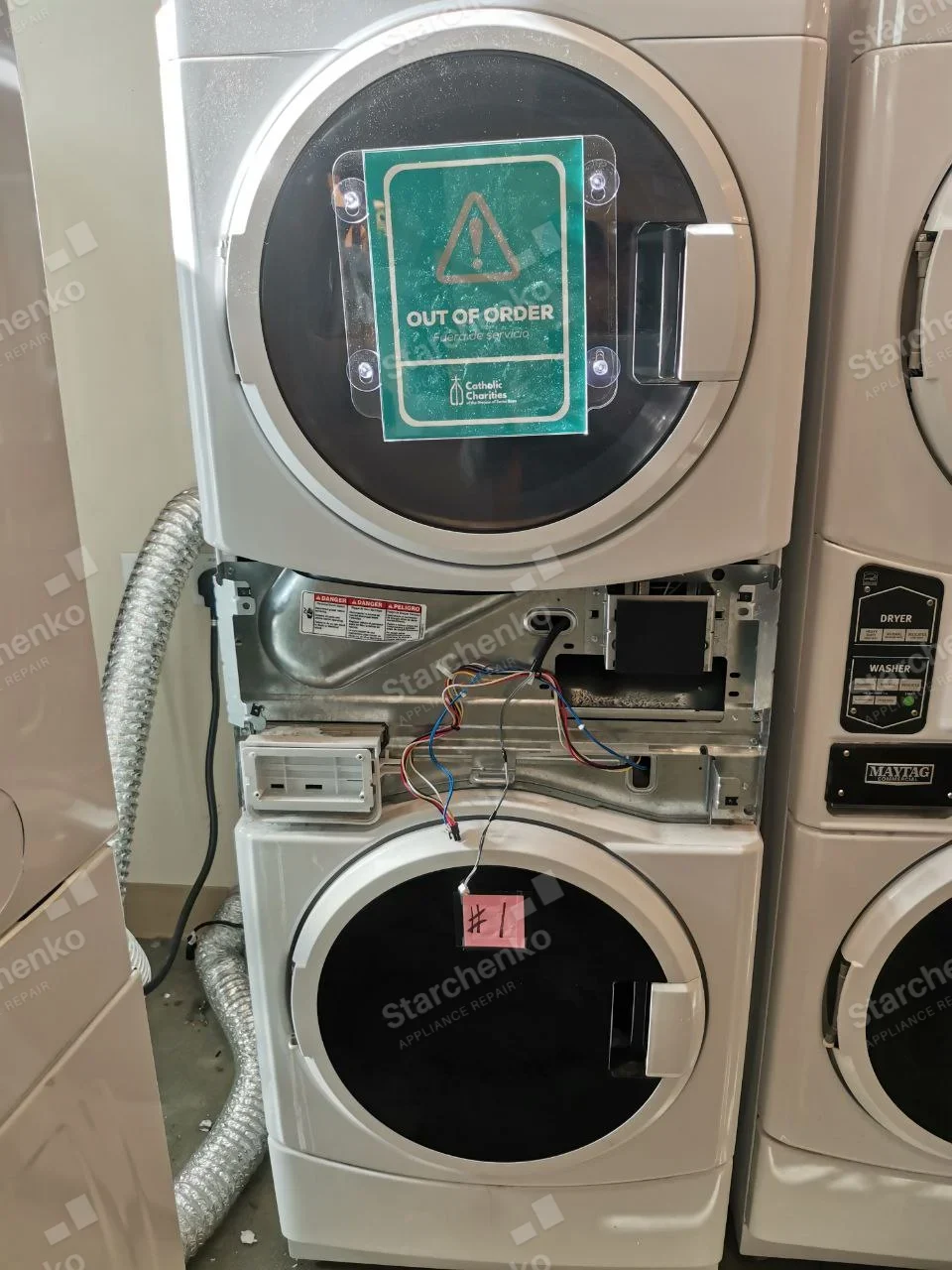 Milnor repair: Stacked laundry pair with lower washer control fascia removed and wiring exposed below dryer.
