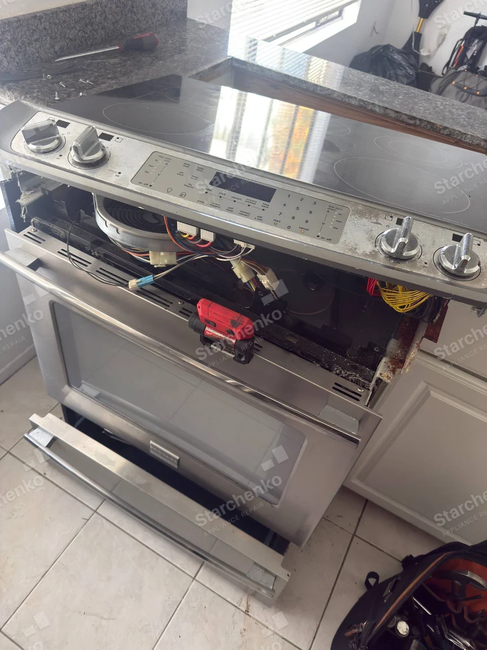 FRIGIDAIRE badge centered on main range oven-door handle, control fascia opened to expose wiring.
