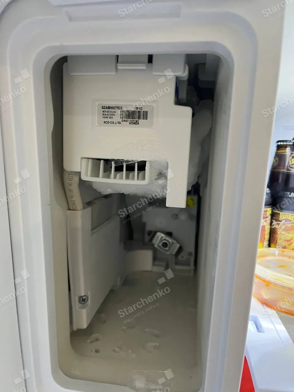Whirlpool repair: Open refrigerator ice-maker compartment with frost around the internal assembly.