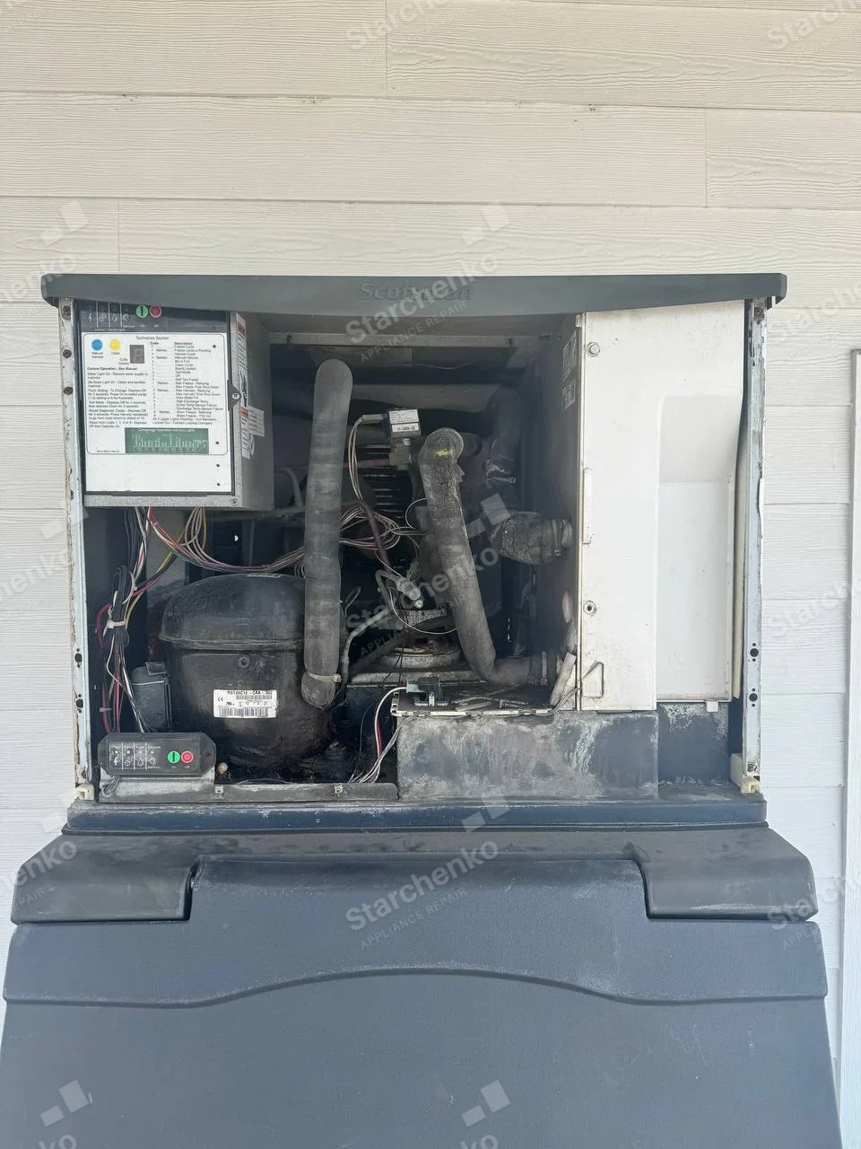 Scotsman word molded into upper front trim above exposed compressor and refrigeration system of large ice machine.