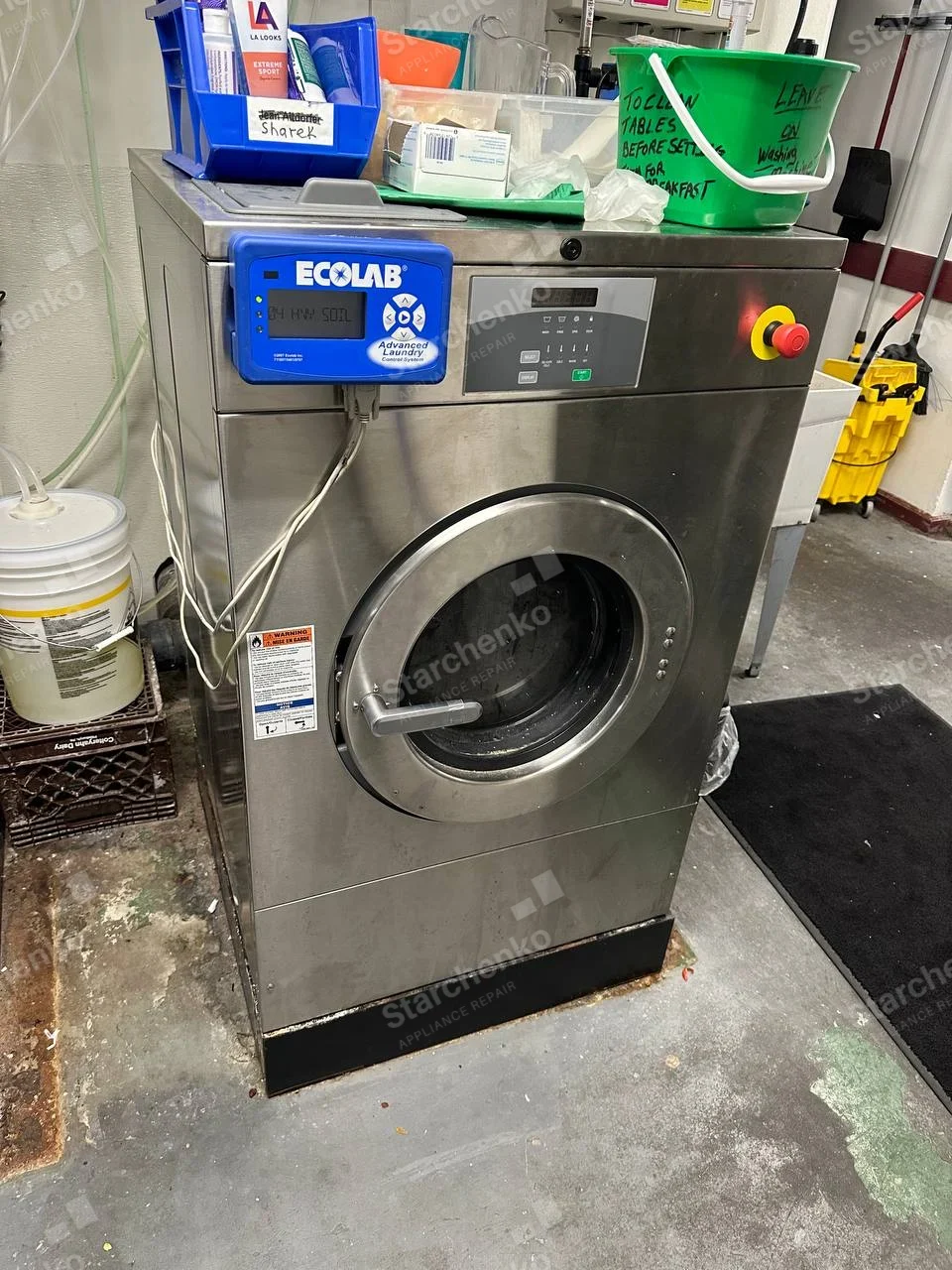 Continental Girbau repair: Large stainless industrial front-load washer with separate Ecolab chemical controller mounted on left, no machine brand visible.