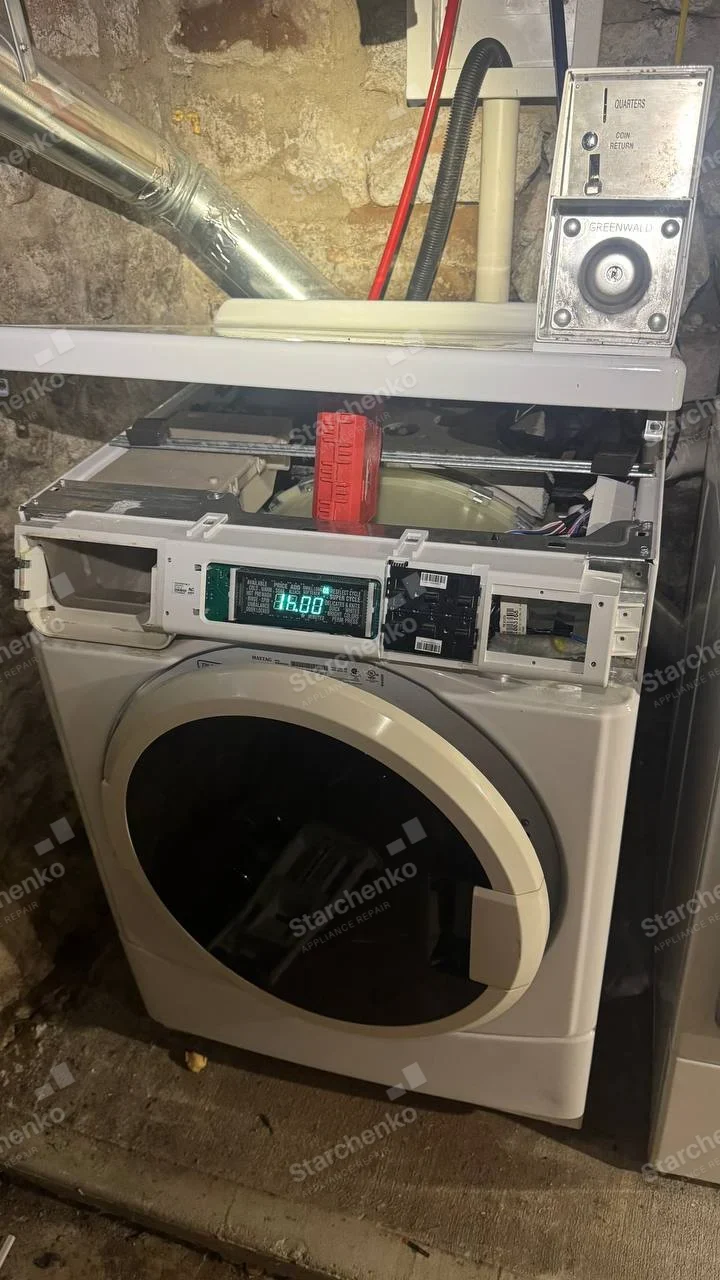 Huebsch repair: Coin-operated front-loading laundry dryer with vent duct above, top control fascia removed and electronics exposed, GREENWALD badge on coin mechanism only.