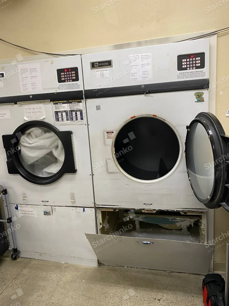 Maytag Commercial repair: Maytag brand plaque on the right of two adjacent commercial dryers, right dryer has open drum door and lower service panel.