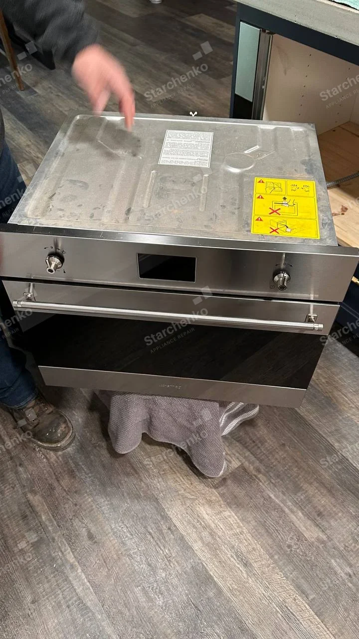 Samsung repair: Stainless built-in oven removed from cabinet on padded stand, manufacturer inscription on lower fascia not legible.