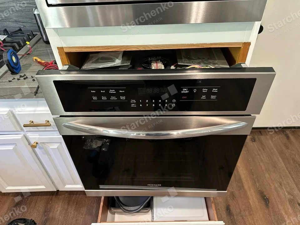 Frigidaire built-in oven with upper control trim raised and wiring visible in the gap.