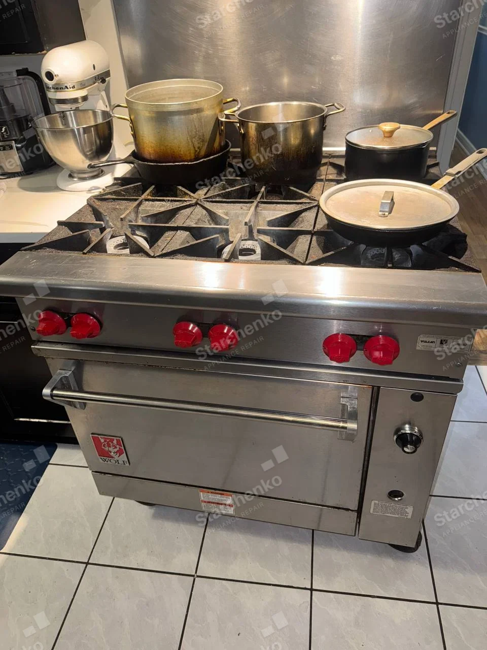 Wolf crest and word on oven door of six-burner gas range, kitchen setting, no opened service panel visible.