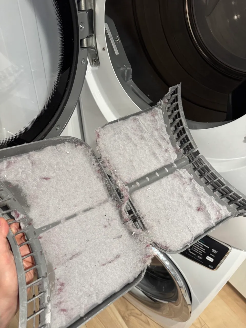 Dryer lint filter packed solid with lint, held up in front of the open door