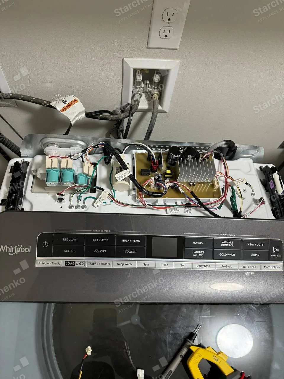 Whirlpool wordmark on control panel of top-load washer, controls opened showing wiring and board.