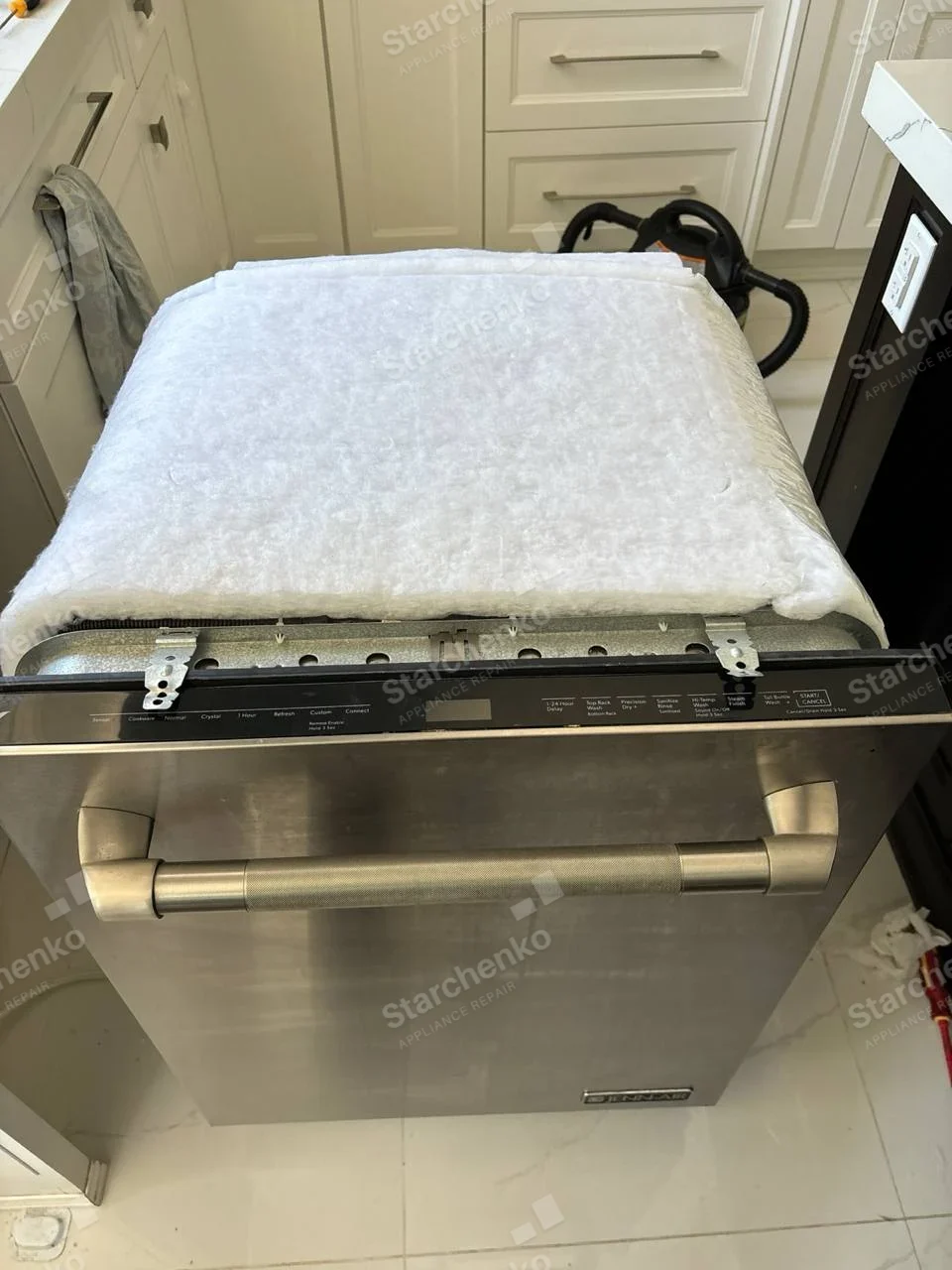 Stainless built-in dishwasher pulled forward with insulation exposed, MAYTAG brand plate on lower door.